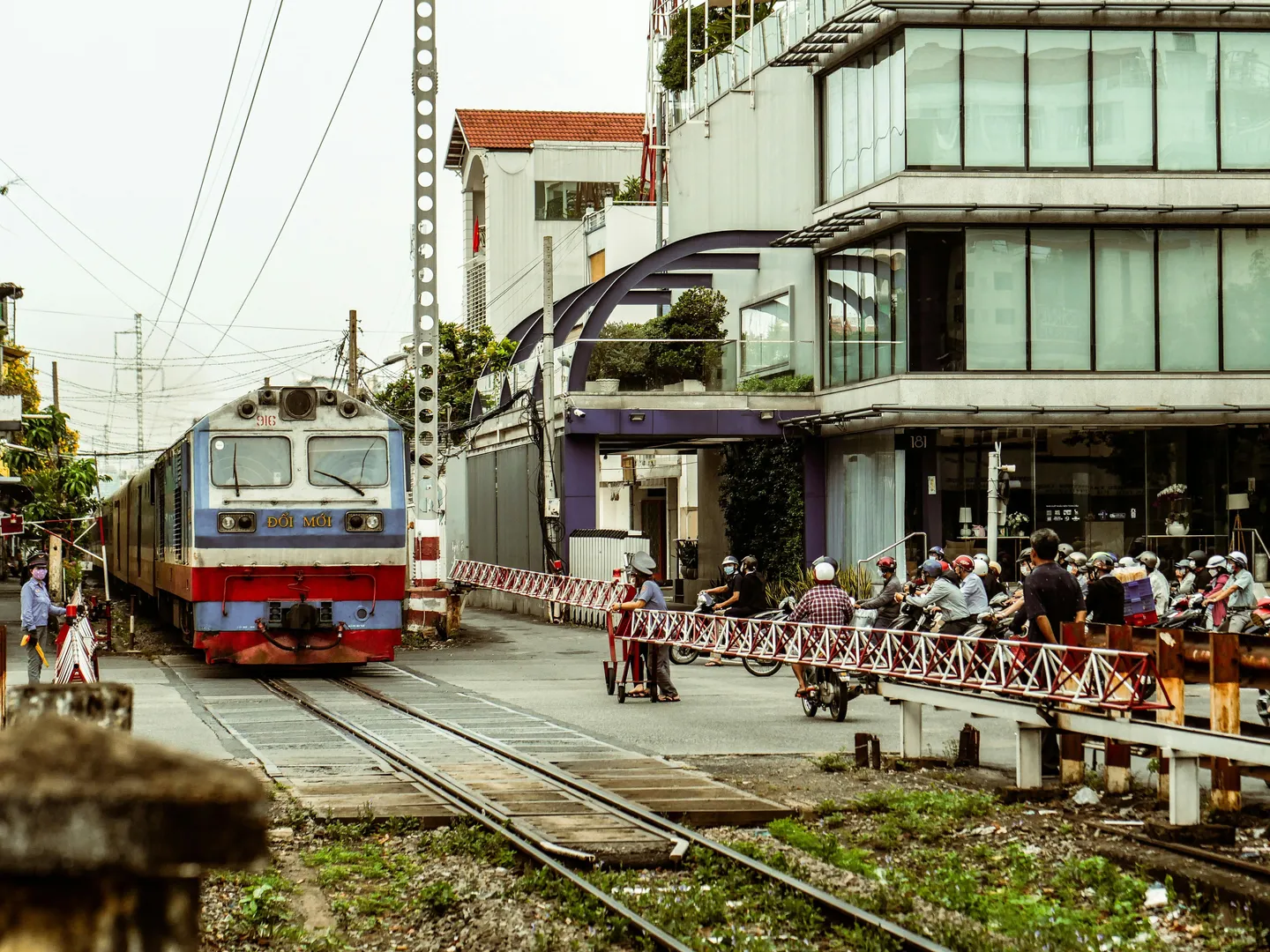 Voyage en Asie — train local traversant une rue urbaine au Vietnam avec passage à niveau et scooters attendant le train