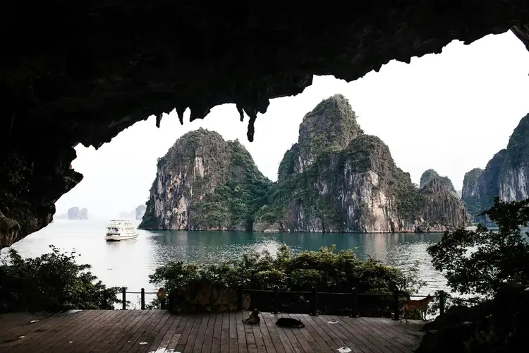 Voyage au Vietnam — Vue de la Baie d’Ha Long depuis l’intérieur d’une grotte avec stalactites et bateau dans l’eau.