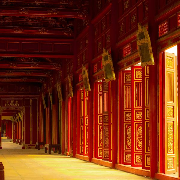 Voyage au Vietnam — Vue d’un couloir rouge et or dans la Cité Impériale de Hué, lumière naturelle illuminant les dalles et détails sculptés.