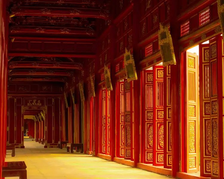 Voyage au Vietnam — Vue d’un couloir rouge et or dans la Cité Impériale de Hué, lumière naturelle illuminant les dalles et détails sculptés.