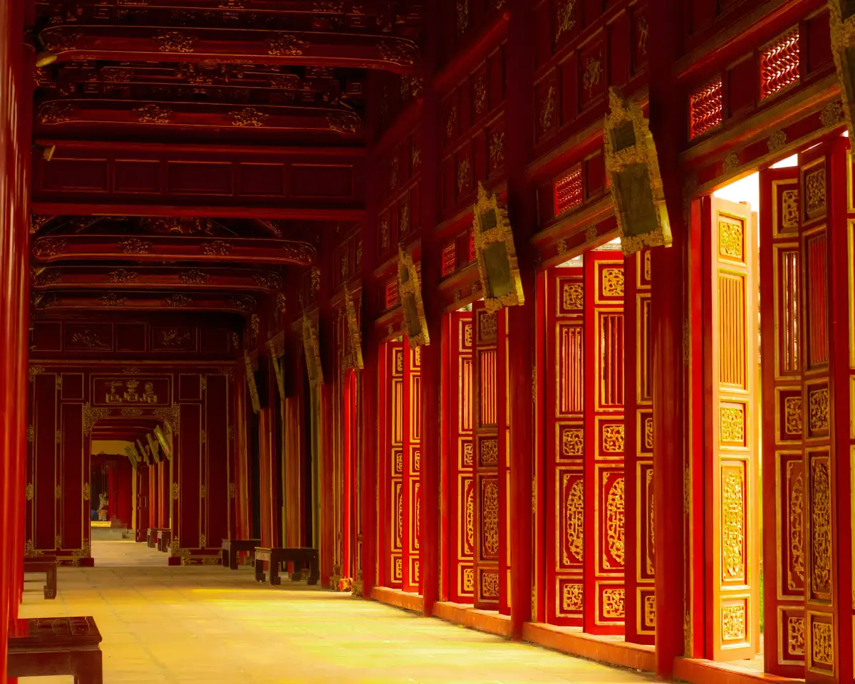 Voyage au Vietnam — Vue d’un couloir rouge et or dans la Cité Impériale de Hué, lumière naturelle illuminant les dalles et détails sculptés.