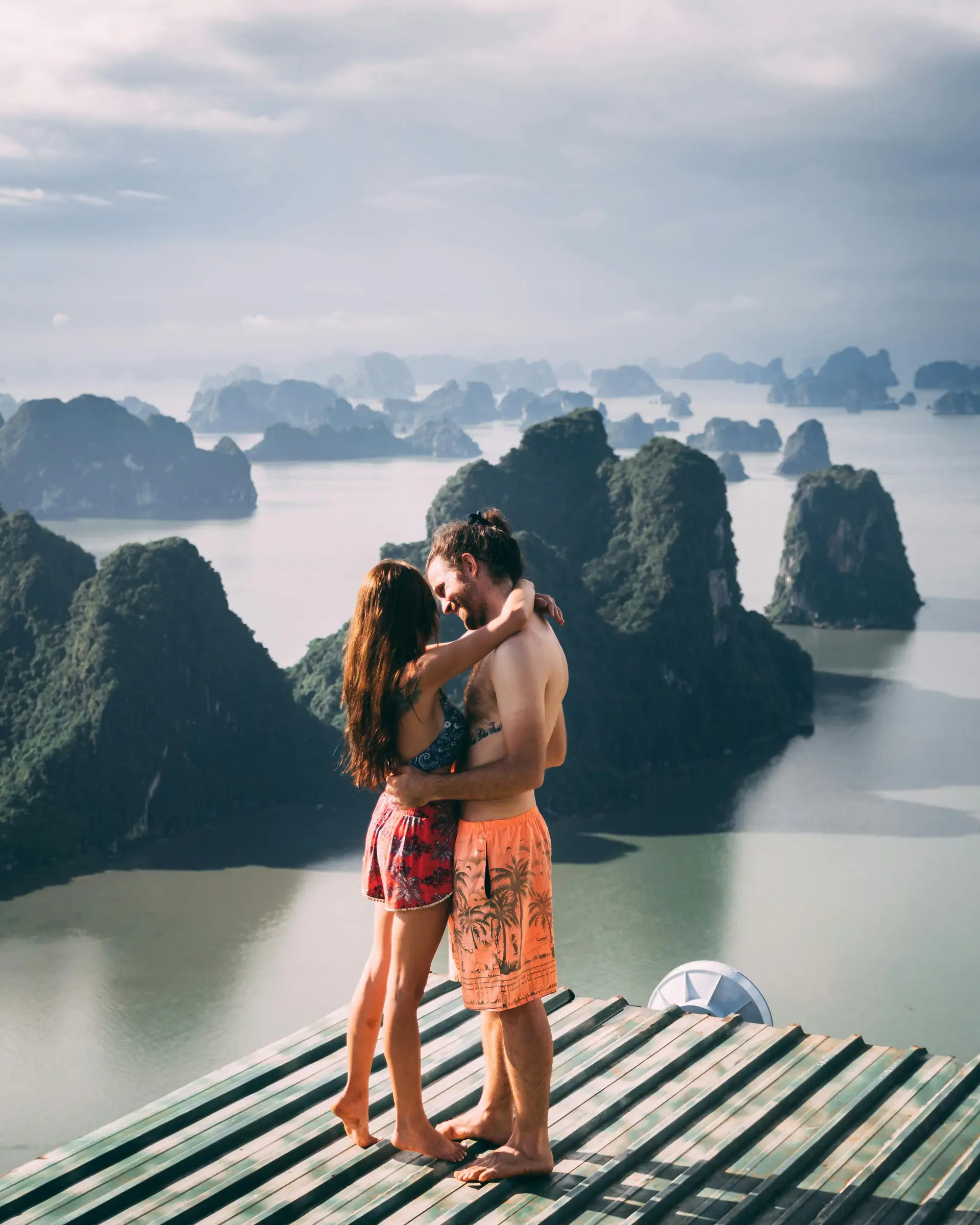 Couple s'enlaçant sur une plateforme en bois offrant une vue panoramique sur les pitons karstiques de la baie de Ha Long.