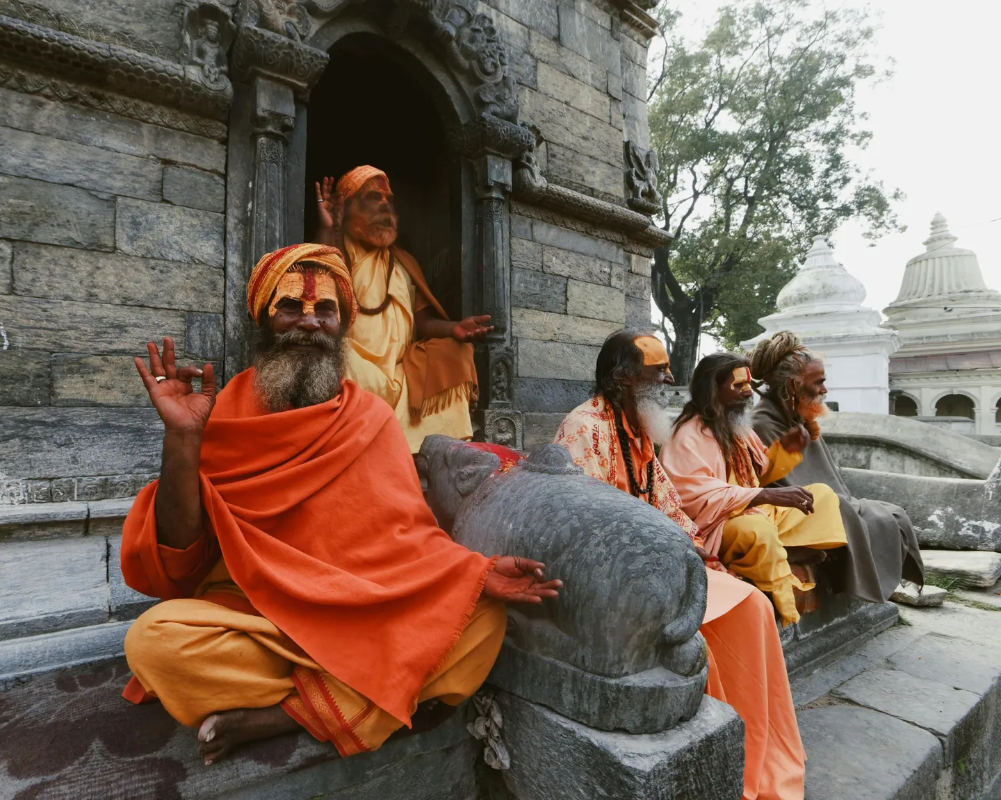Groupe de Sadhus hindous en robes safran et orange assis sur les marches d'un temple en pierre ancienne, avec des peintures faciales rituelles (tilak) et une statue de Nandi au premier plan