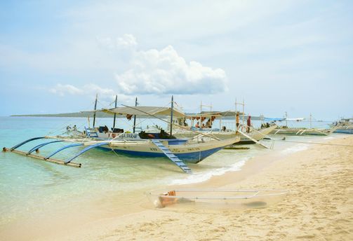 Travel in the Philippines — Traditional Filipino outrigger bangka boats anchored in the clear turquoise waters and white sand beach of Boracay.