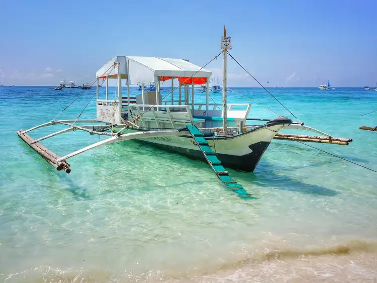 Travel in the Philippines — A traditional wooden Bangka boat anchored in the shallow, clear turquoise waters of Siquijor Island near the beach.