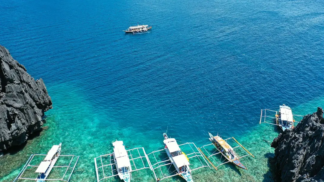 Plusieurs bateaux traditionnels Bangka ancrés dans les eaux turquoise cristallines sur une côte rocheuse à Palawan.