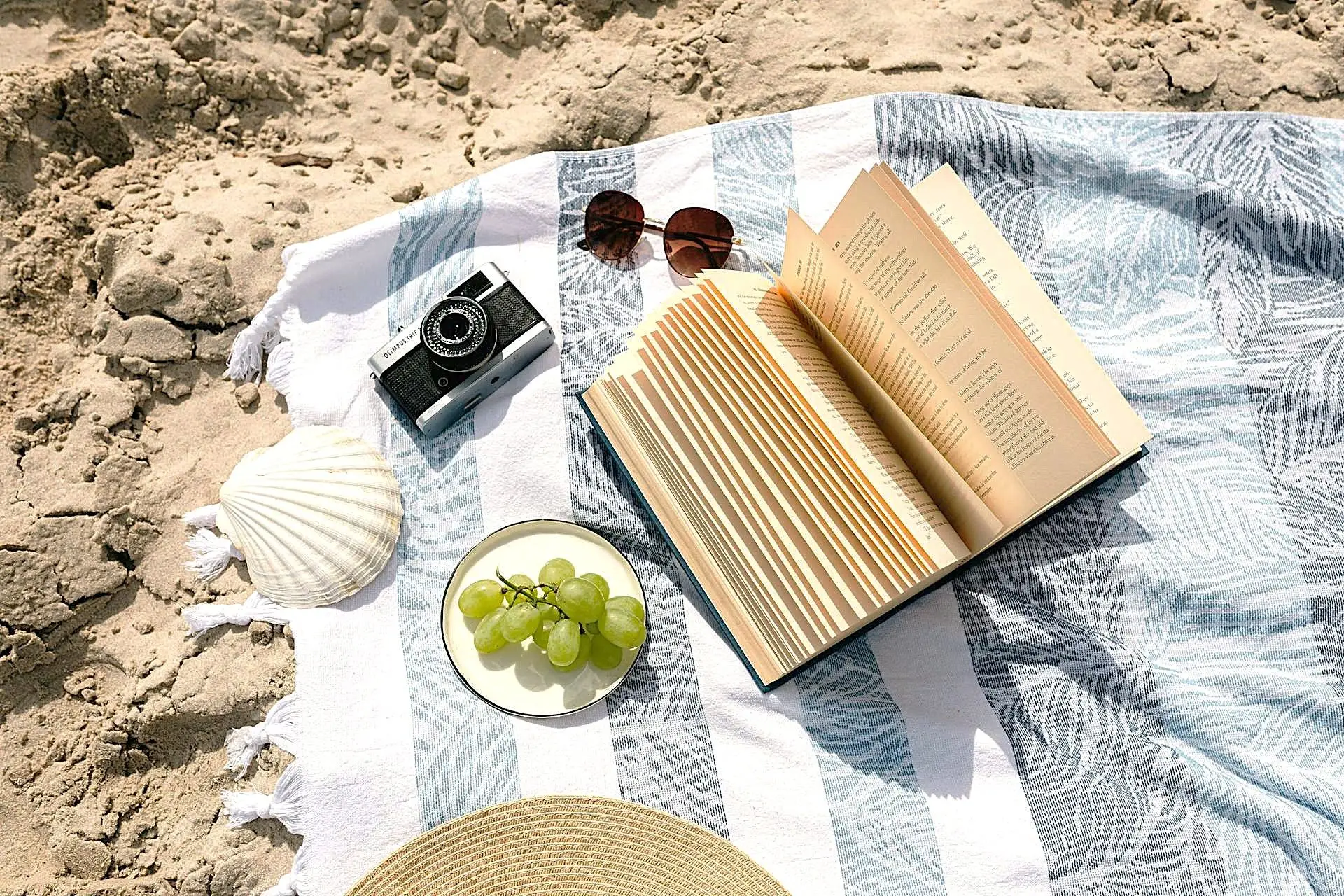 Travel in the Philippines — Open book and sunglasses resting on a striped blanket on a white sand beach in Palawan, ready for a calm read.