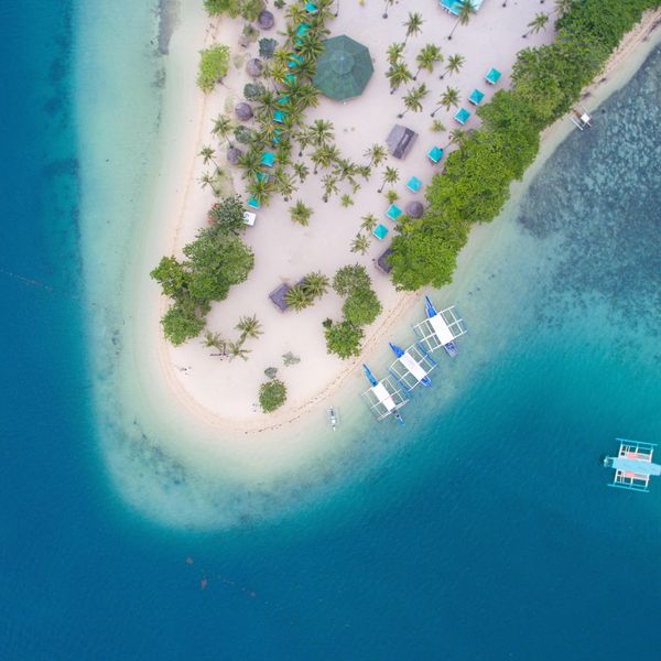 Travel in the Philippines — Aerial view of a pristine island in the Palawan archipelago with traditional boats anchored near the white sand beach.