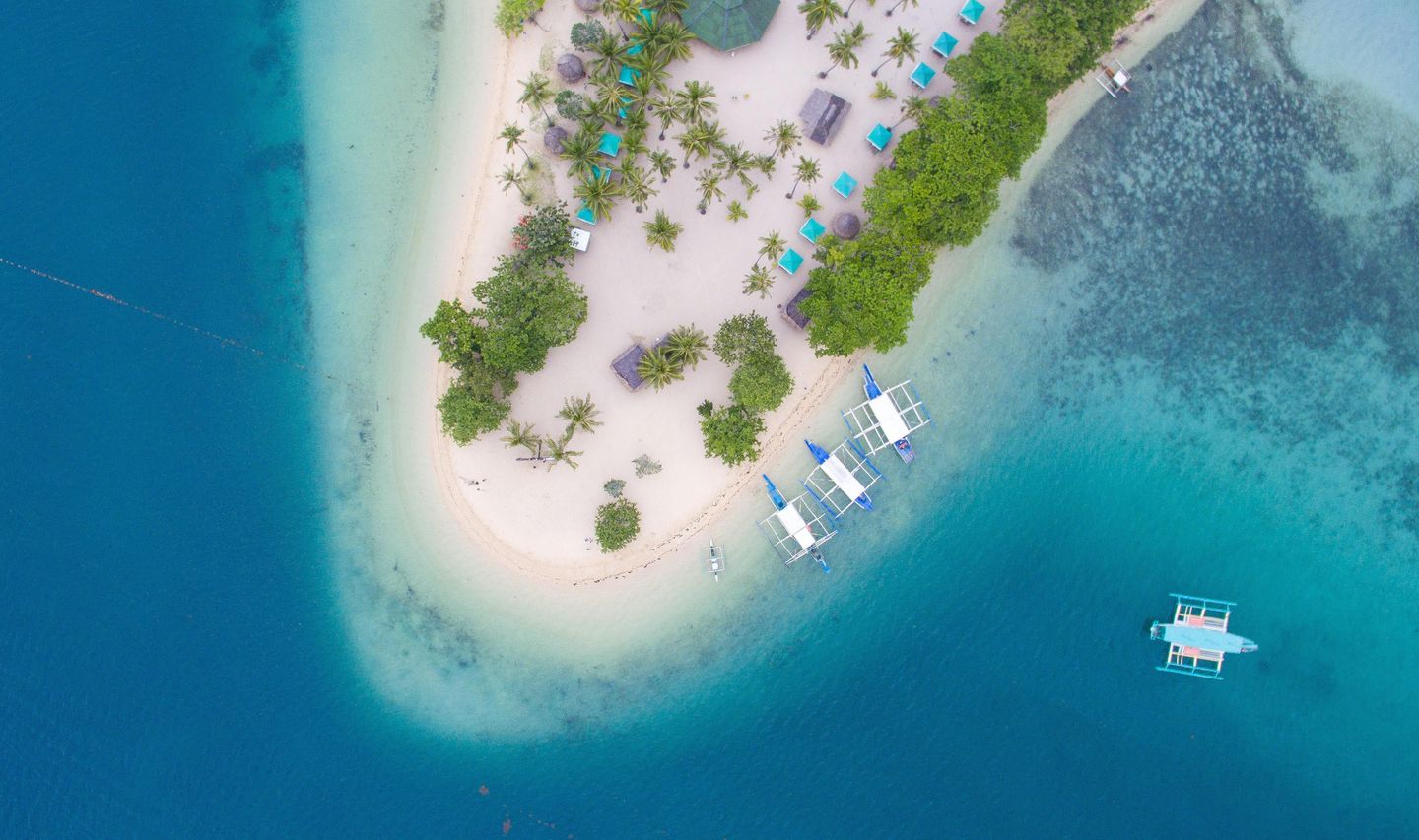 Travel in the Philippines — Aerial view of a pristine island in the Palawan archipelago with traditional boats anchored near the white sand beach.