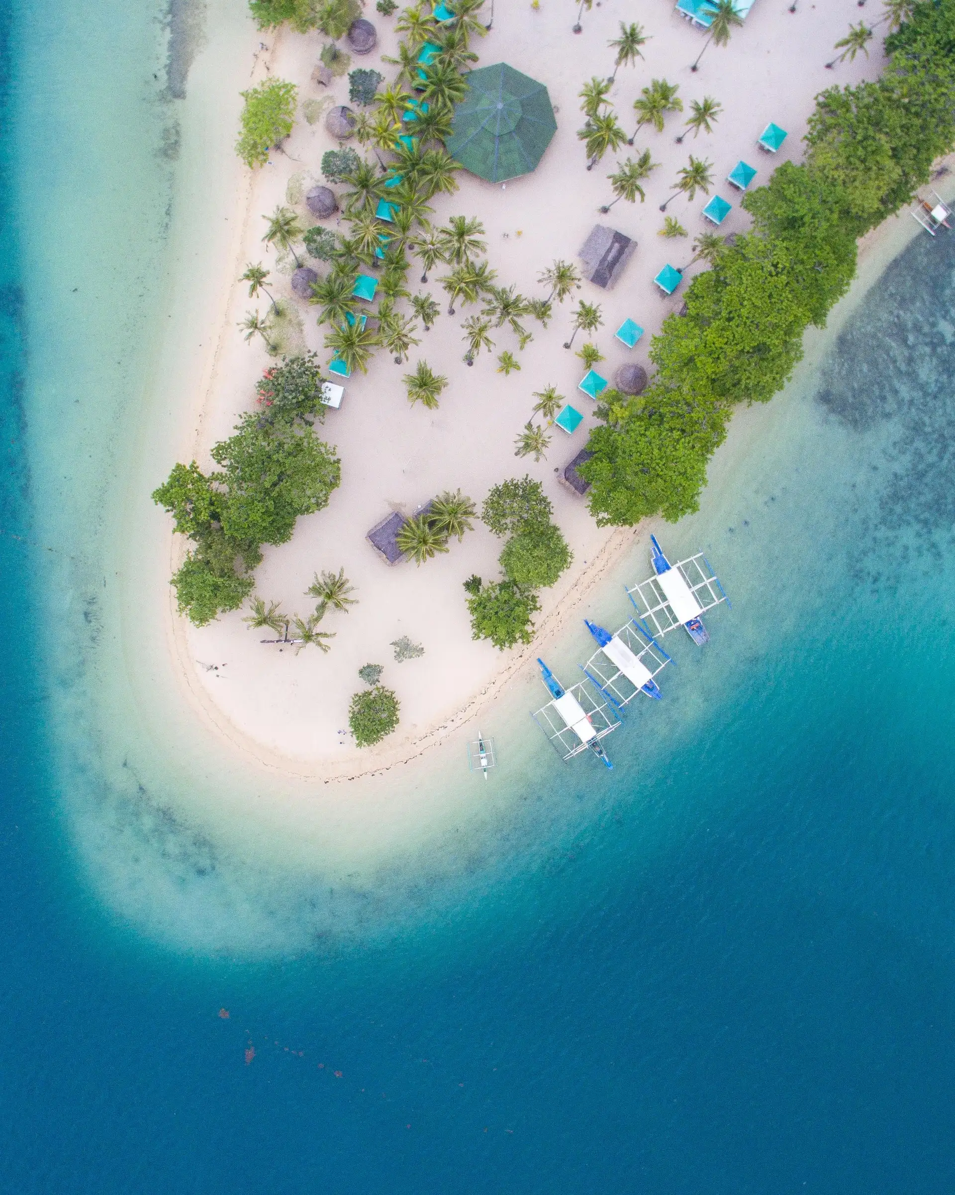 Travel in the Philippines — Aerial view of a pristine island in the Palawan archipelago with traditional boats anchored near the white sand beach.
