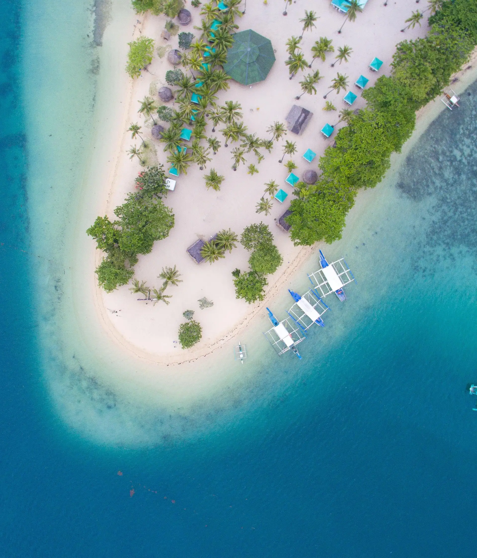 Travel in the Philippines — Aerial view of a pristine island in the Palawan archipelago with traditional boats anchored near the white sand beach.