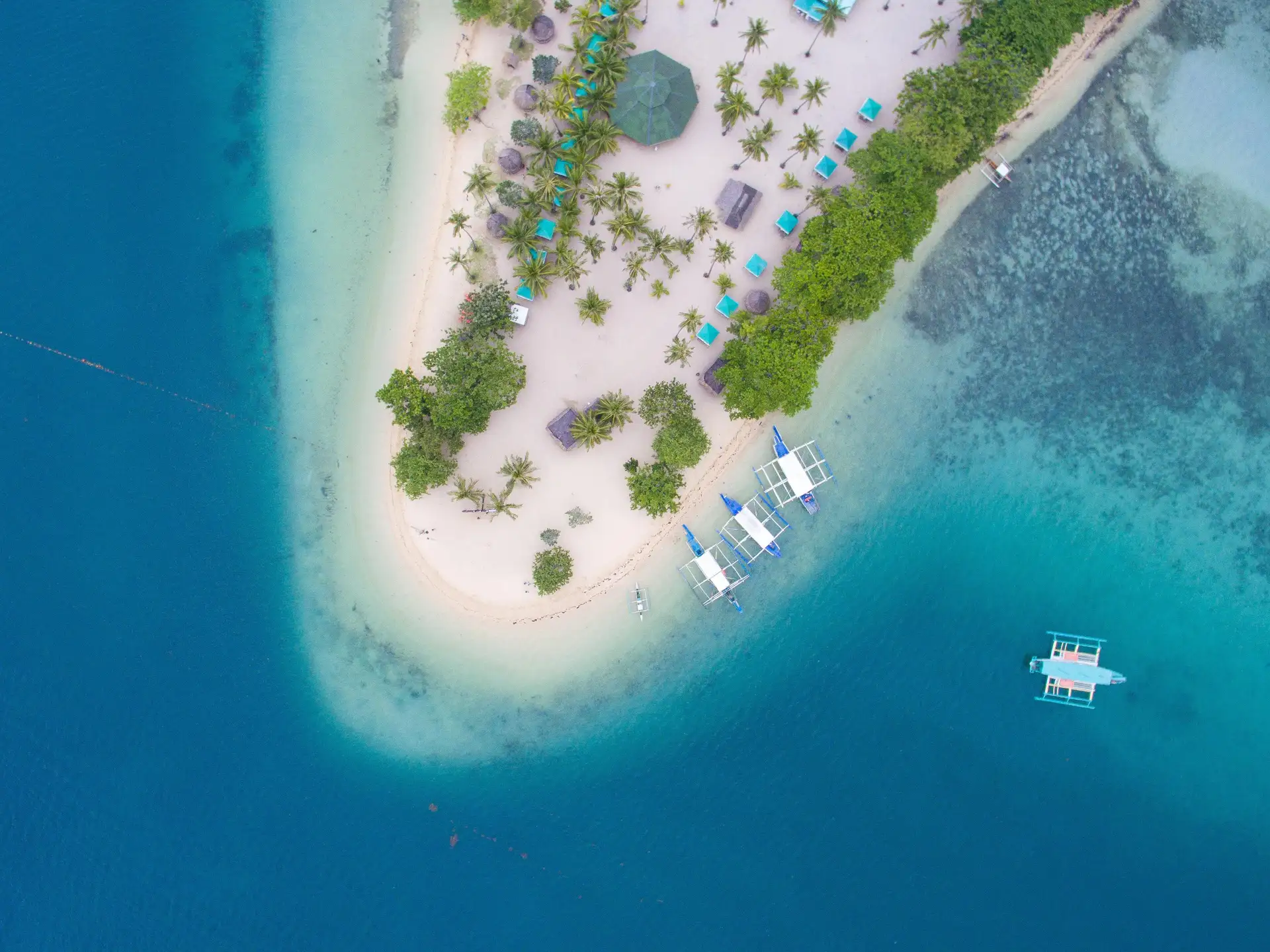 Travel in the Philippines — Aerial view of a pristine island in the Palawan archipelago with traditional boats anchored near the white sand beach.