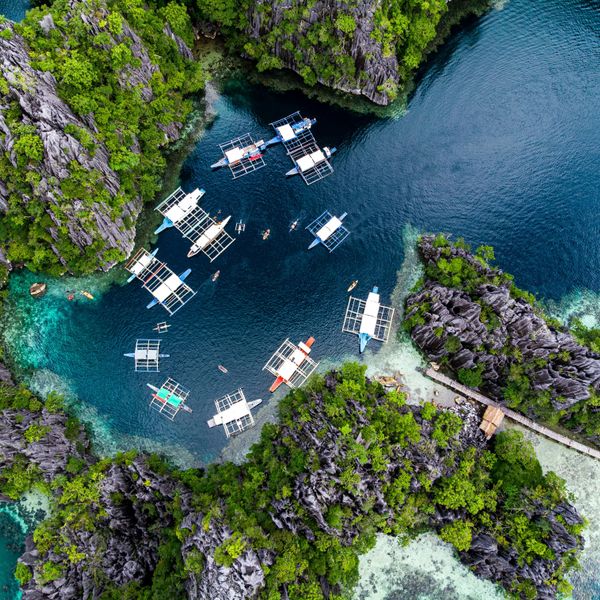 Travel in the Philippines — Aerial view of traditional Bangka boats anchored in a hidden lagoon surrounded by steep limestone karst in Palawan.