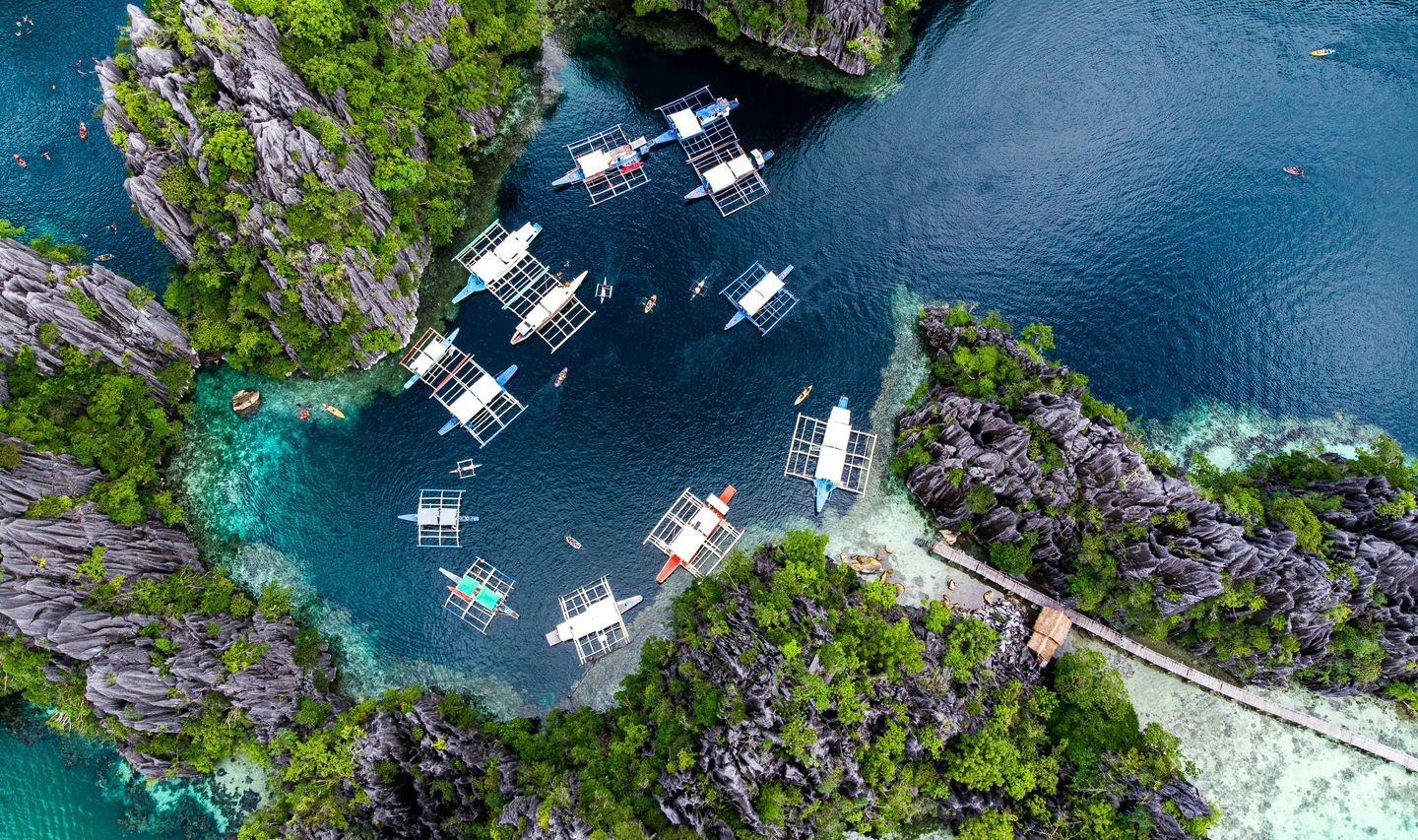 Travel in the Philippines — Aerial view of traditional Bangka boats anchored in a hidden lagoon surrounded by steep limestone karst in Palawan.