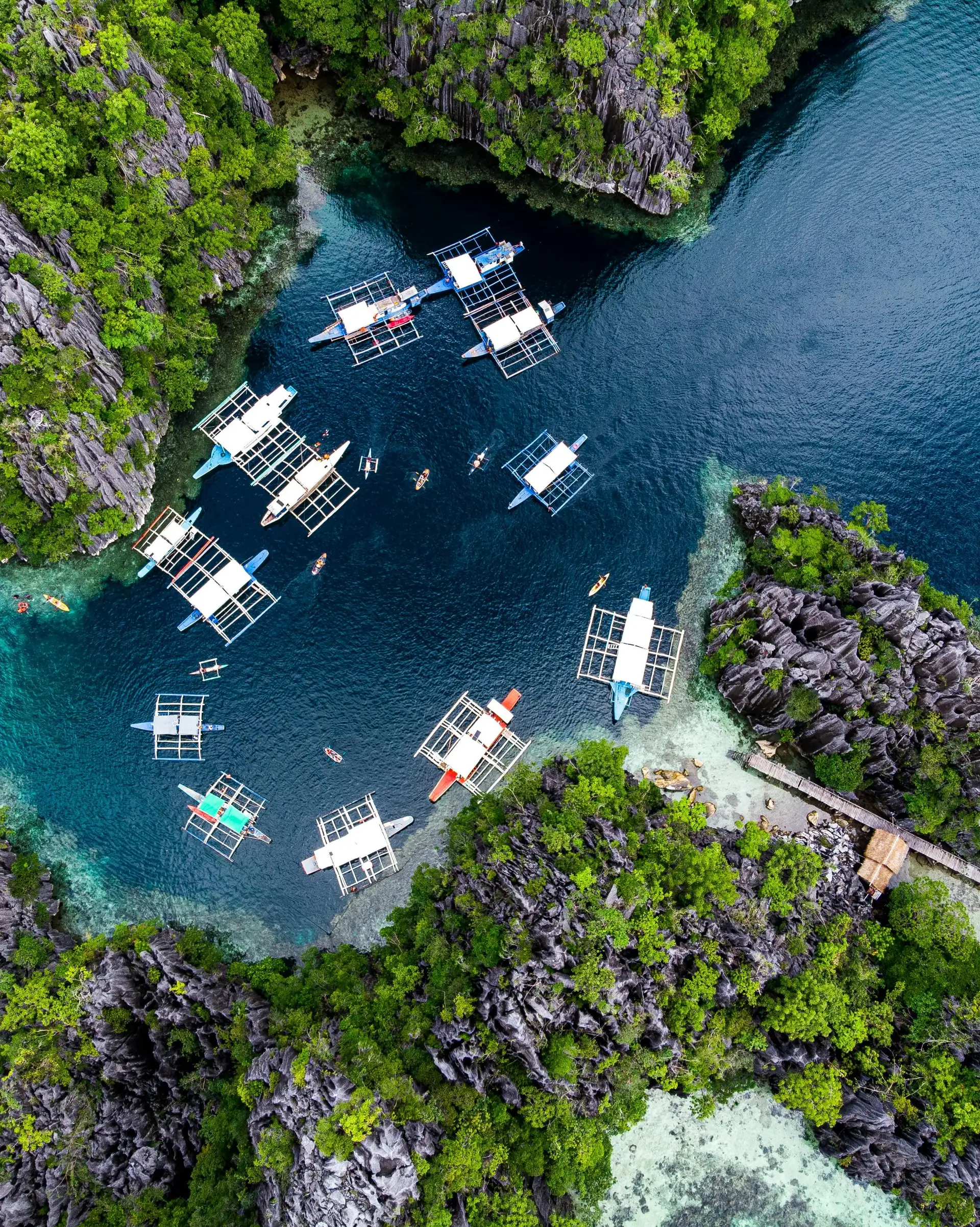 Travel in the Philippines — Aerial view of traditional Bangka boats anchored in a hidden lagoon surrounded by steep limestone karst in Palawan.
