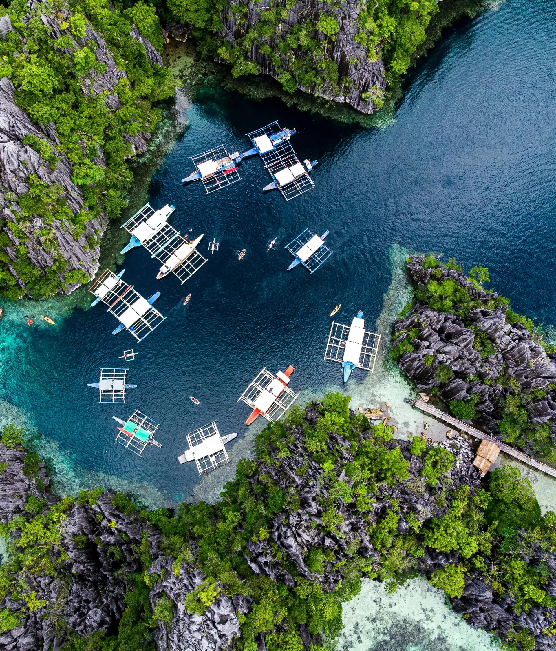 Travel in the Philippines — Aerial view of traditional Bangka boats anchored in a hidden lagoon surrounded by steep limestone karst in Palawan.