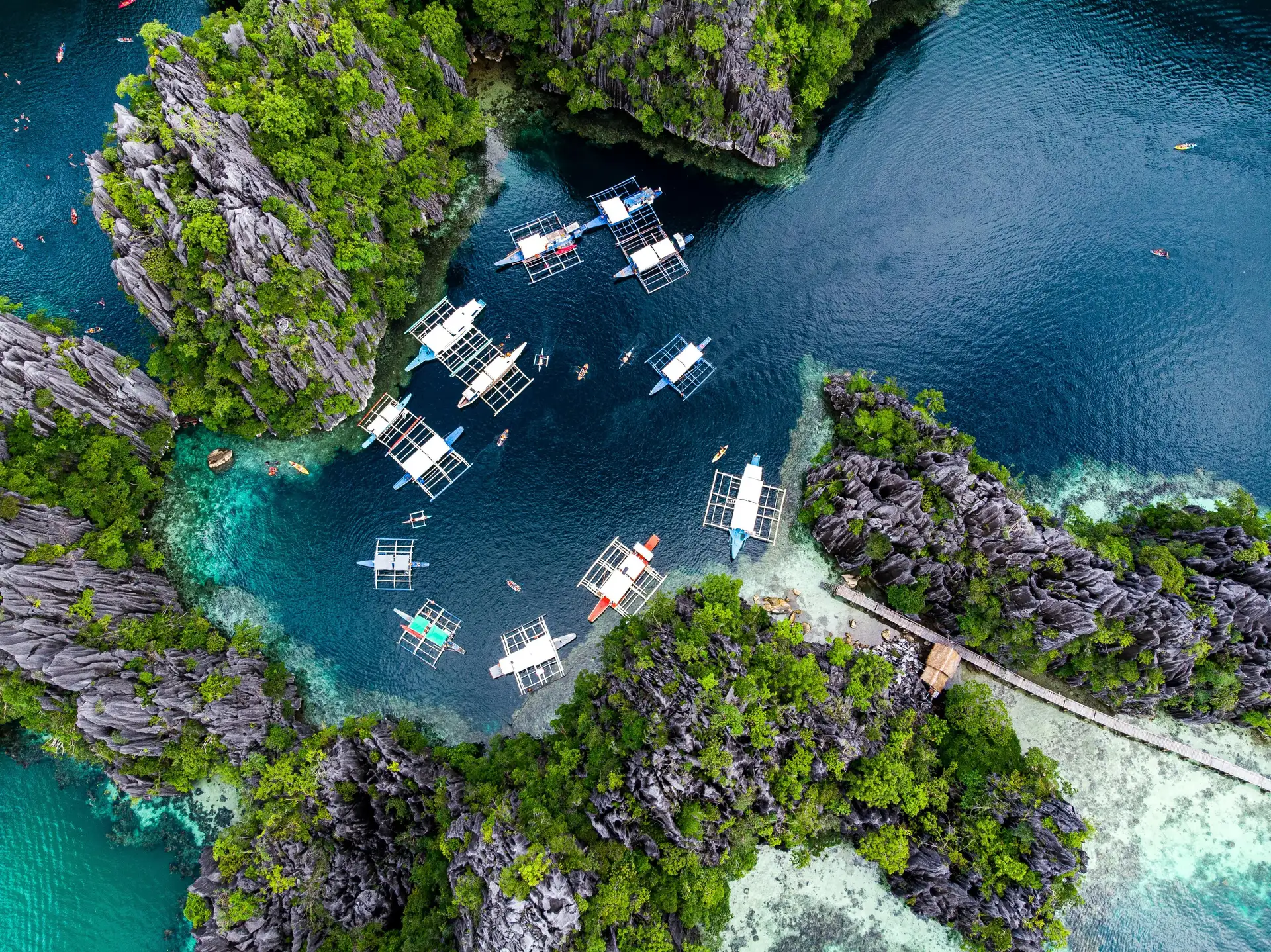 Travel in the Philippines — Aerial view of traditional Bangka boats anchored in a hidden lagoon surrounded by steep limestone karst in Palawan.