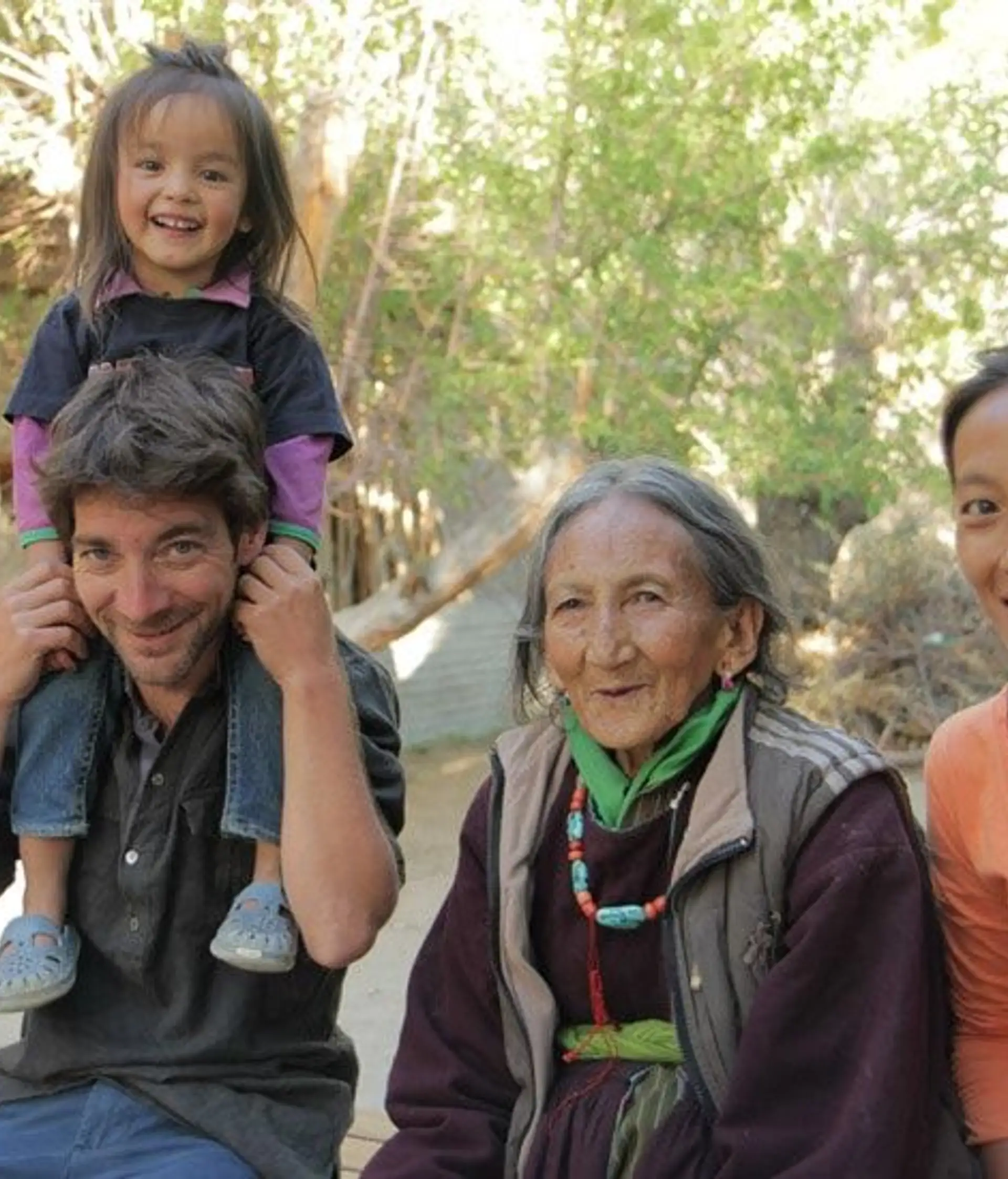 Travel in Asia - Group of people sitting outdoors, smiling together, with a child sitting on an adult’s shoulders