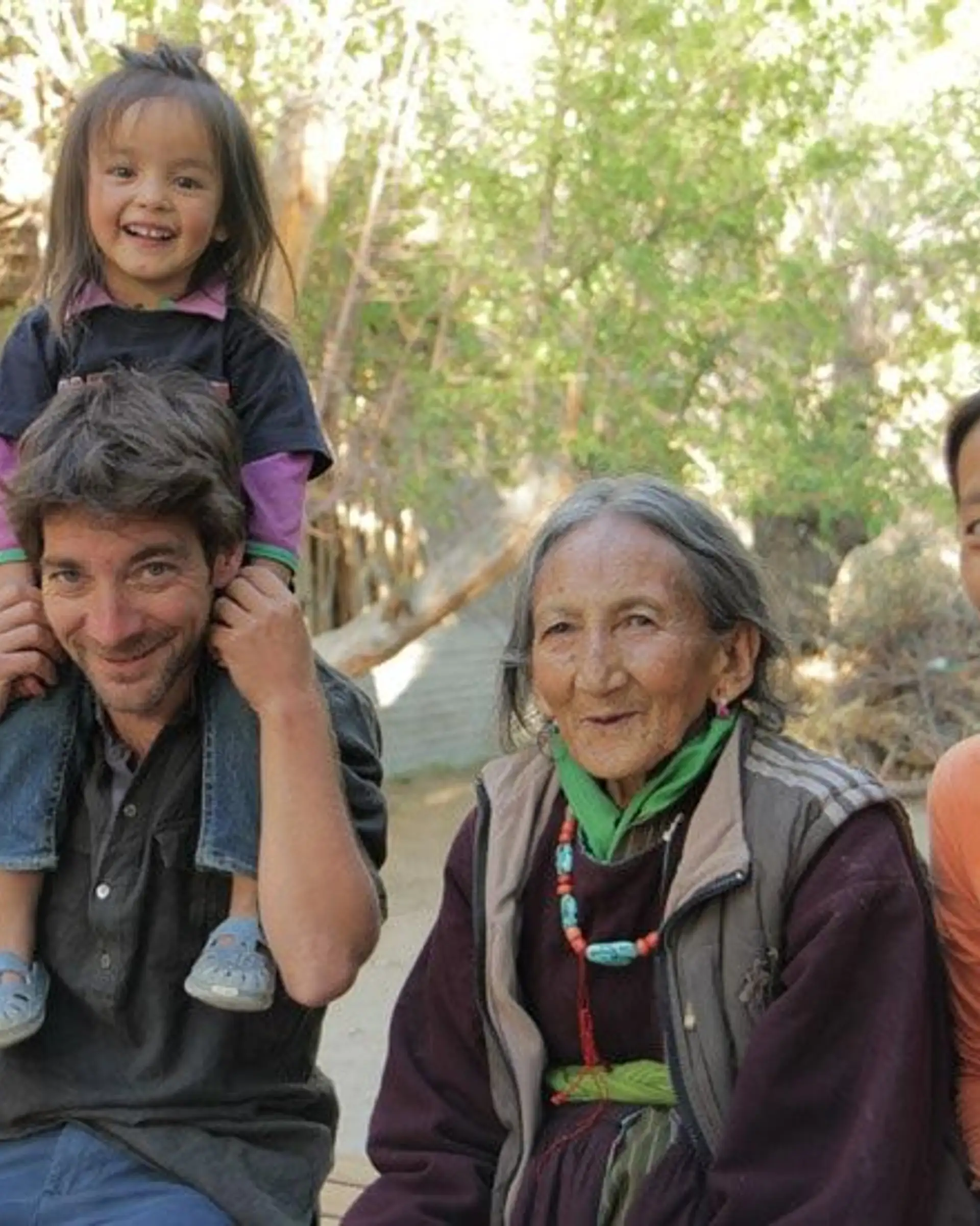 Travel in Asia - Group of people sitting outdoors, smiling together, with a child sitting on an adult’s shoulders