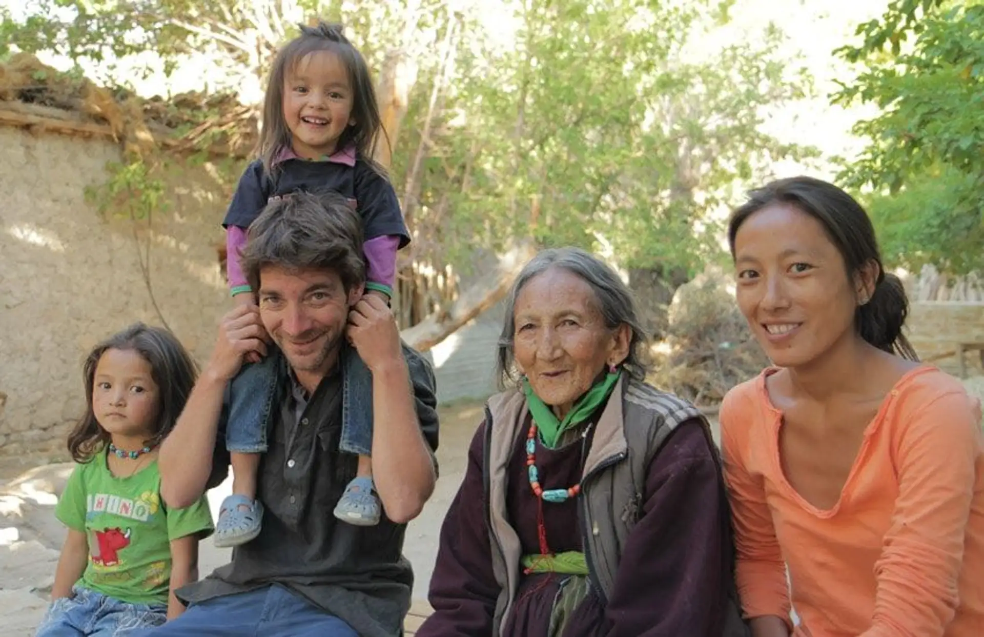 Travel in Asia - Group of people sitting outdoors, smiling together, with a child sitting on an adult’s shoulders