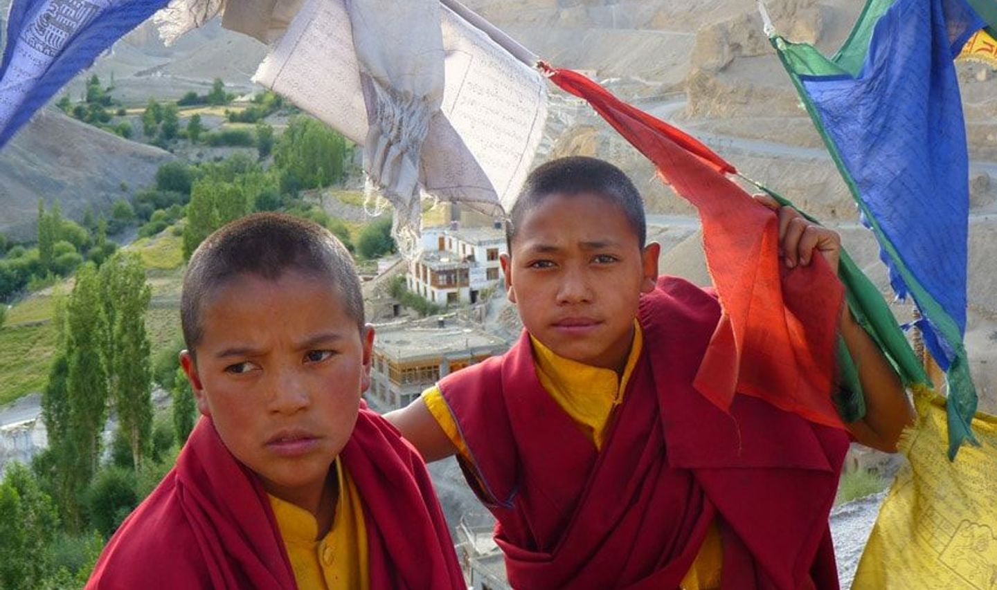 Travel in Asia - Two young Buddhist monks in traditional clothes standing between prayer flags blowing in the wind