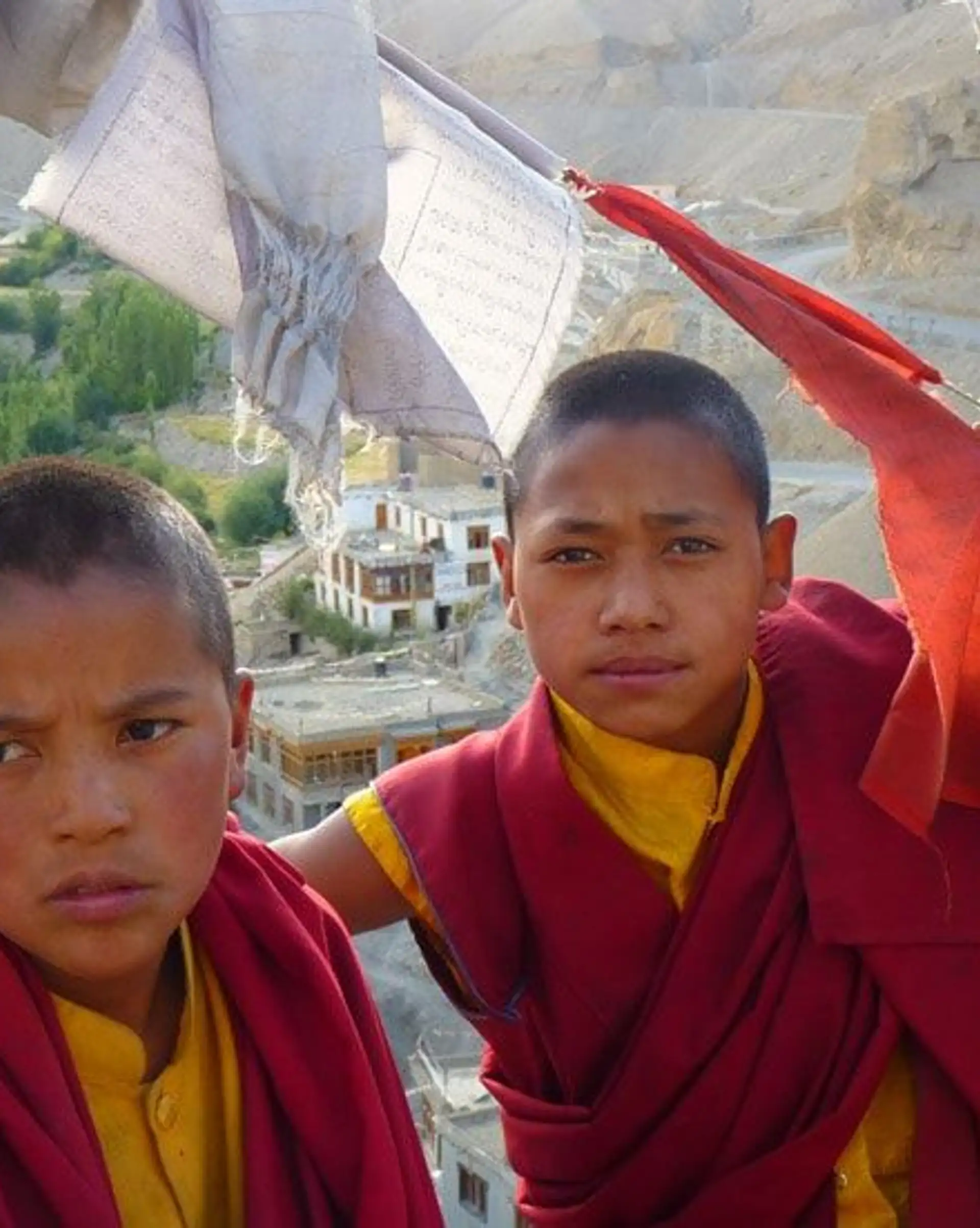 Travel in Asia - Two young Buddhist monks in traditional clothes standing between prayer flags blowing in the wind