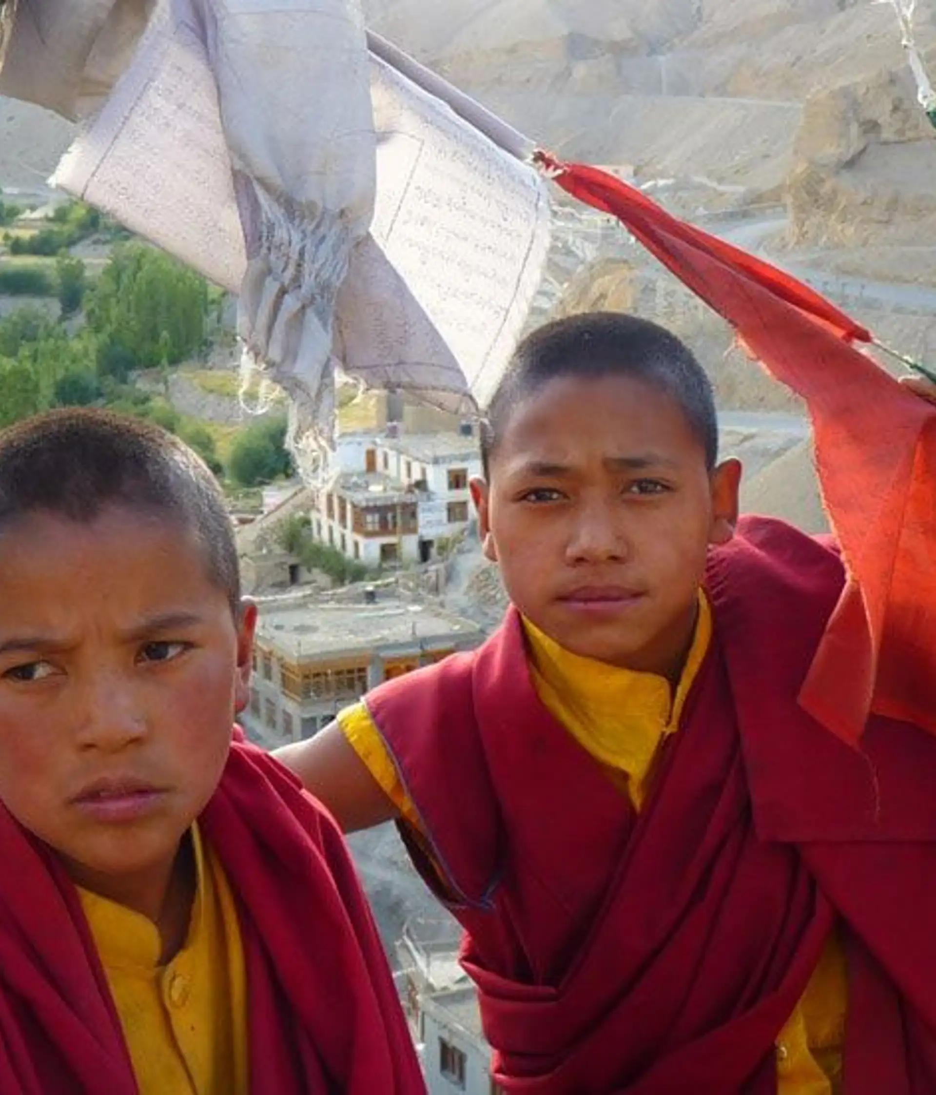 Travel in Asia - Two young Buddhist monks in traditional clothes standing between prayer flags blowing in the wind