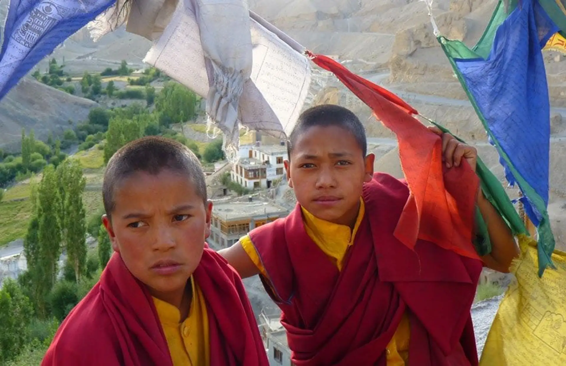Travel in Asia - Two young Buddhist monks in traditional clothes standing between prayer flags blowing in the wind
