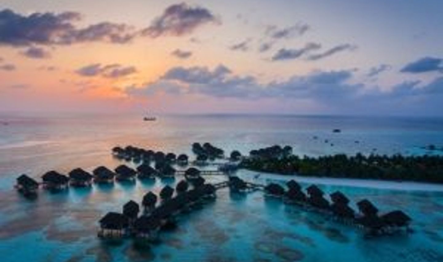 Travel in Asia - Rows of luxury bungalows built on stilts above the clear light blue ocean water of the Maldives