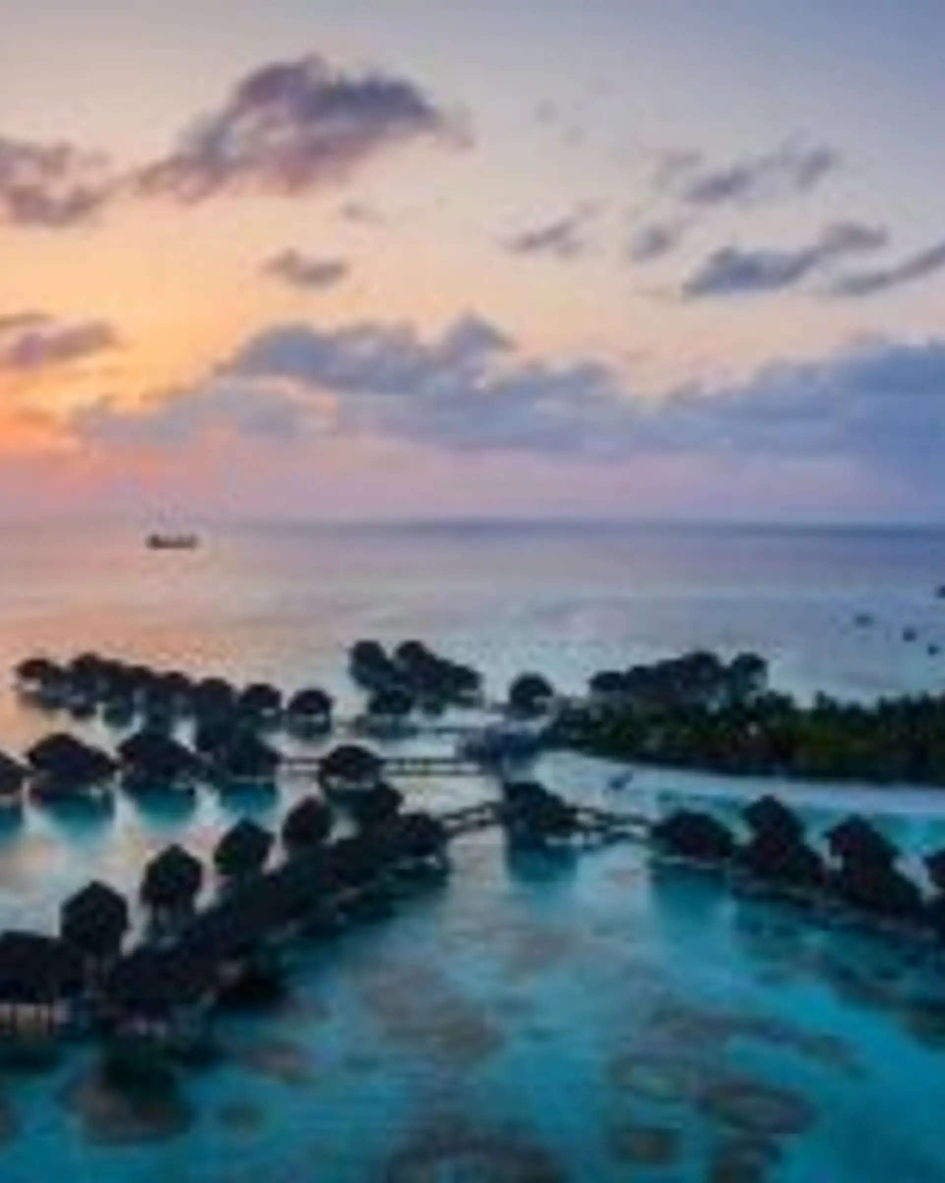 Travel in Asia - Rows of luxury bungalows built on stilts above the clear light blue ocean water of the Maldives