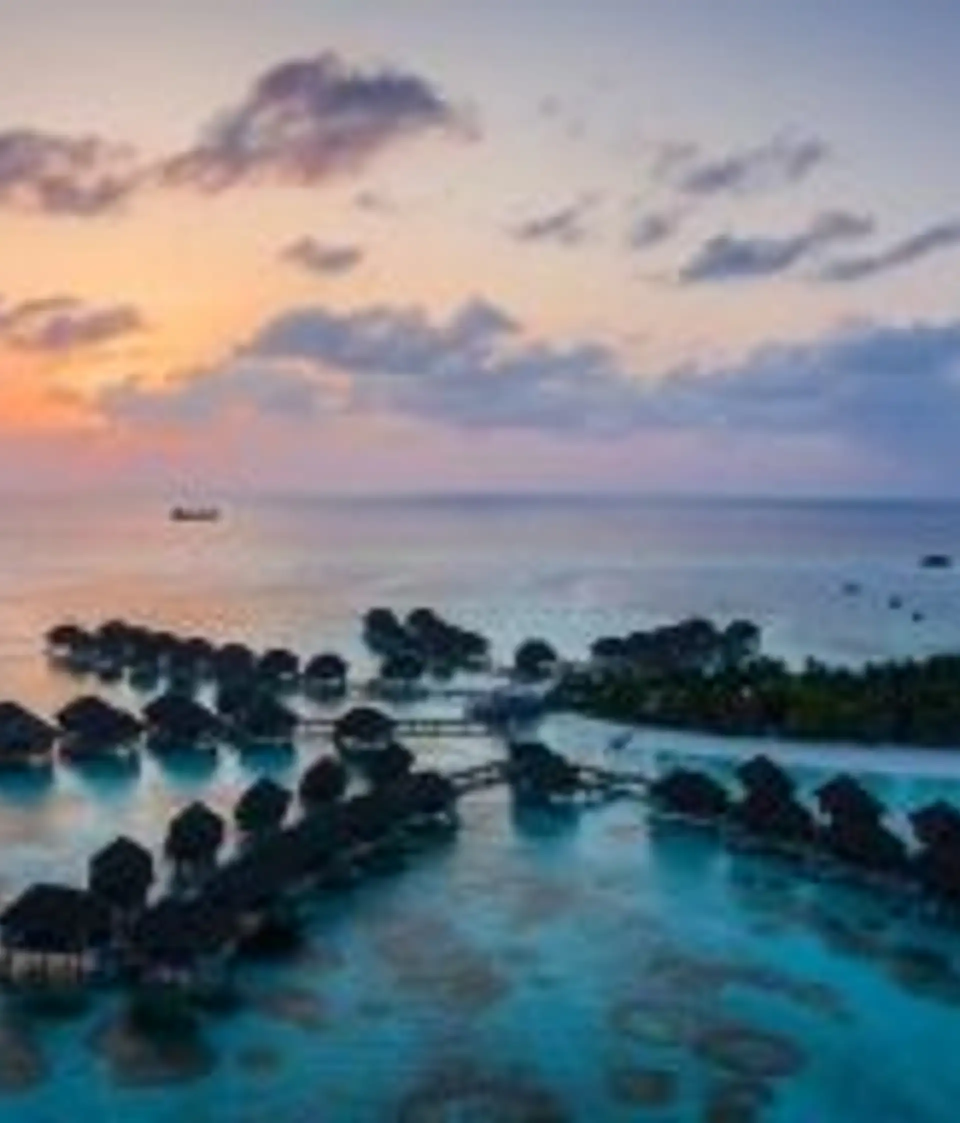 Travel in Asia - Rows of luxury bungalows built on stilts above the clear light blue ocean water of the Maldives