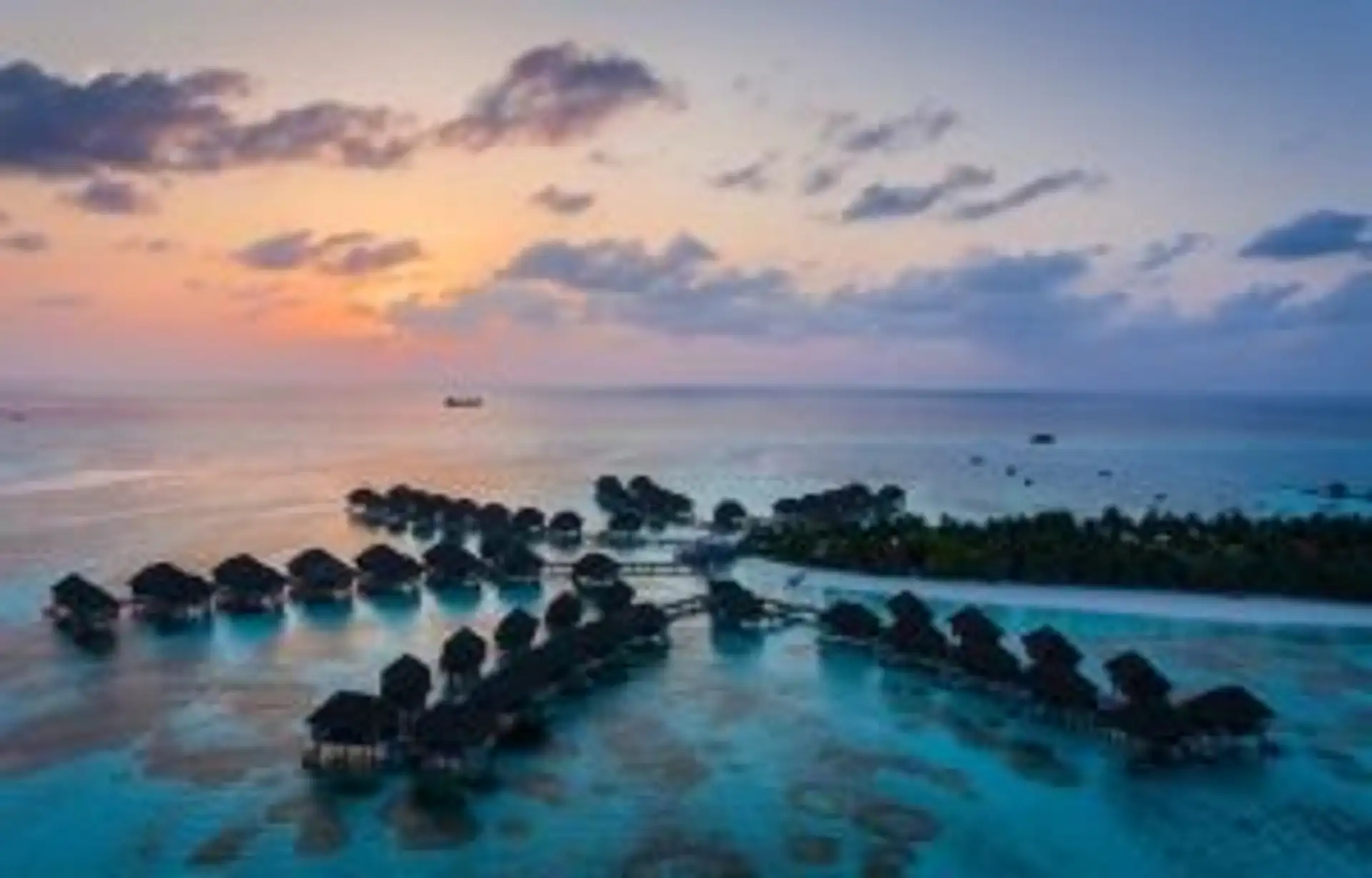 Travel in Asia - Rows of luxury bungalows built on stilts above the clear light blue ocean water of the Maldives