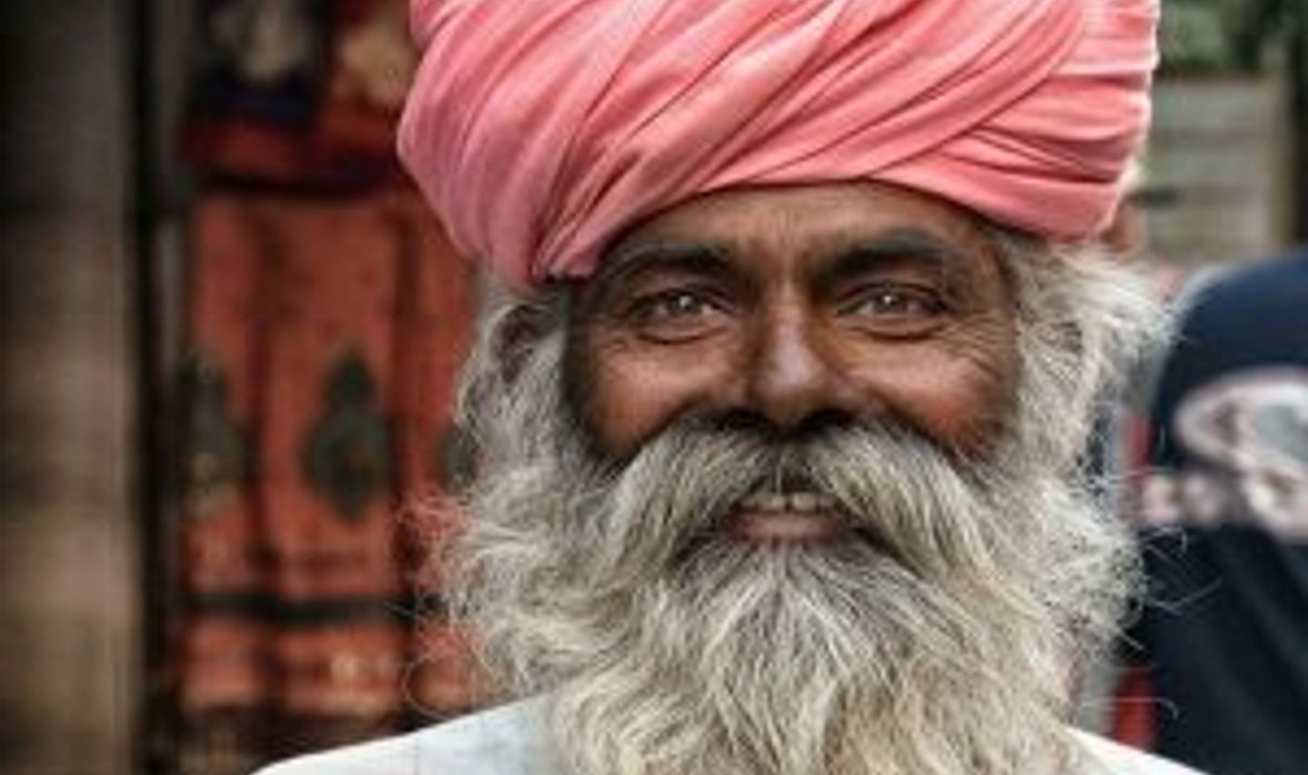 Travel in Asia - Smiling elderly man with a long gray beard wearing a pink turban in India, photographed outdoors