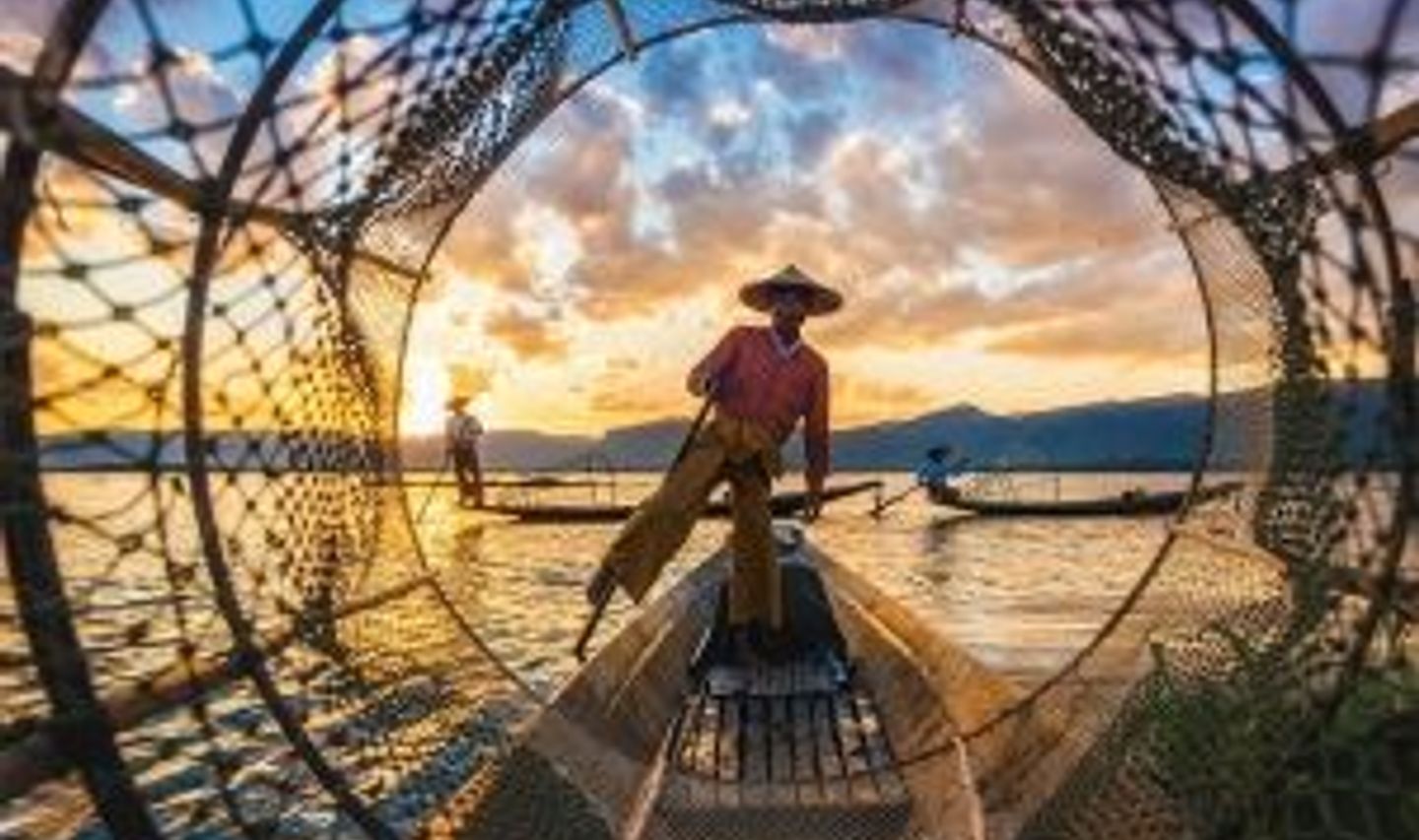 Travel in Asia - Fisherman standing on a wooden boat at sunset, surrounded by fishing nets on calm water