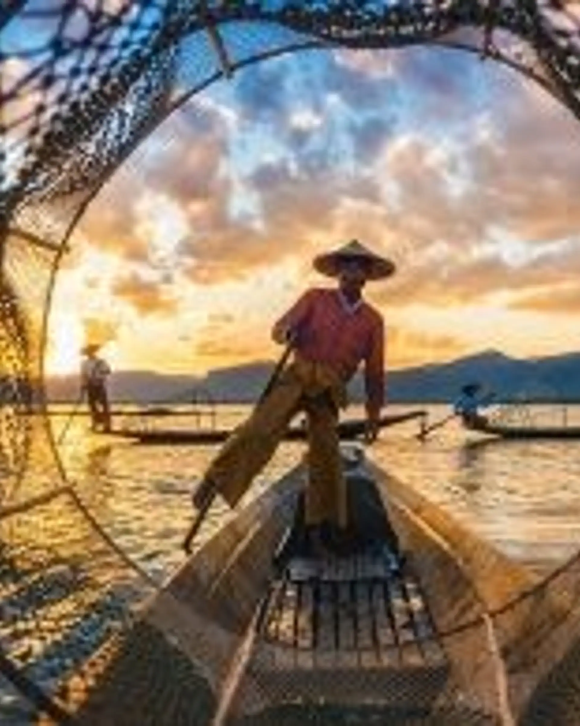 Travel in Asia - Fisherman standing on a wooden boat at sunset, surrounded by fishing nets on calm water