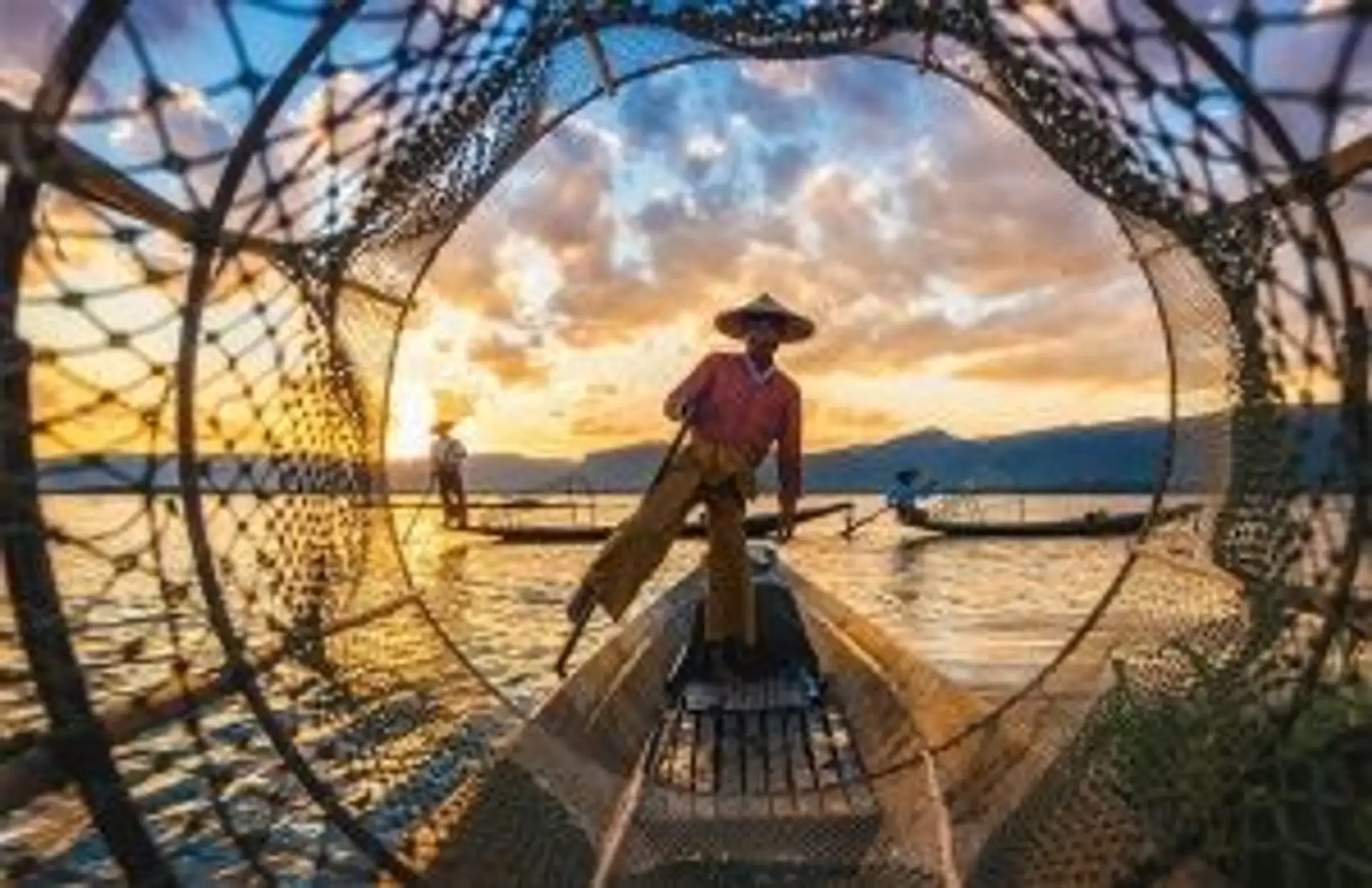 Travel in Asia - Fisherman standing on a wooden boat at sunset, surrounded by fishing nets on calm water