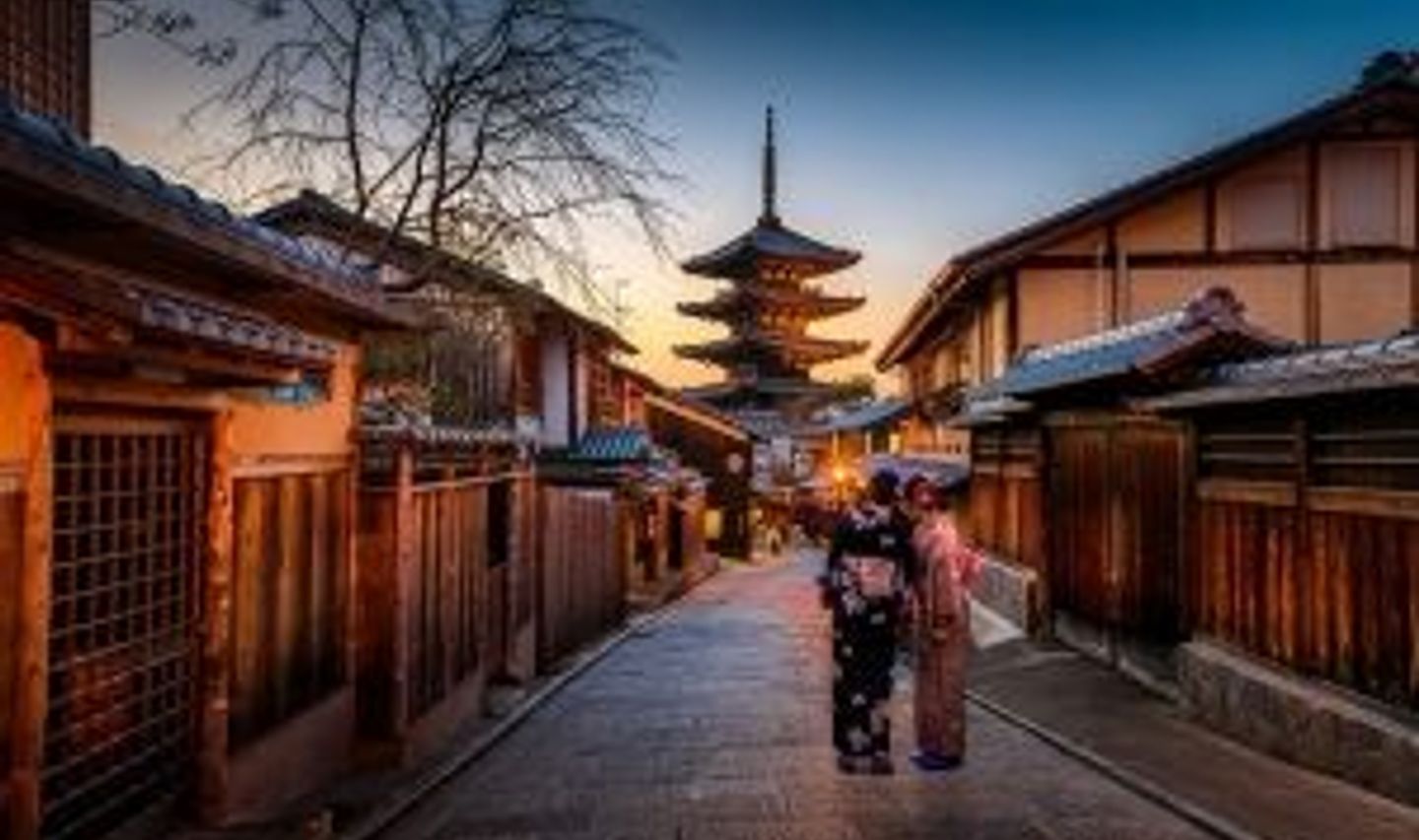 Travel in Asia - Two yukata-clad women standing between traditional wooden fences in the Higashiyama district of Kyoto with the Yasaka Pagoda in the background