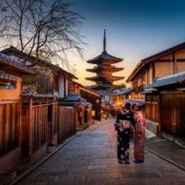 Travel in Asia - Two yukata-clad women standing between traditional wooden fences in the Higashiyama district of Kyoto with the Yasaka Pagoda in the background