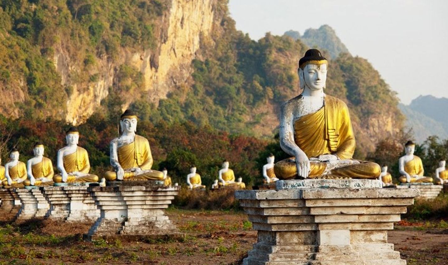 Travel in Asia - Rows of seated Buddha statues in a grassy landscape with rocky hills in the background in Southern Myanmar (Burma)