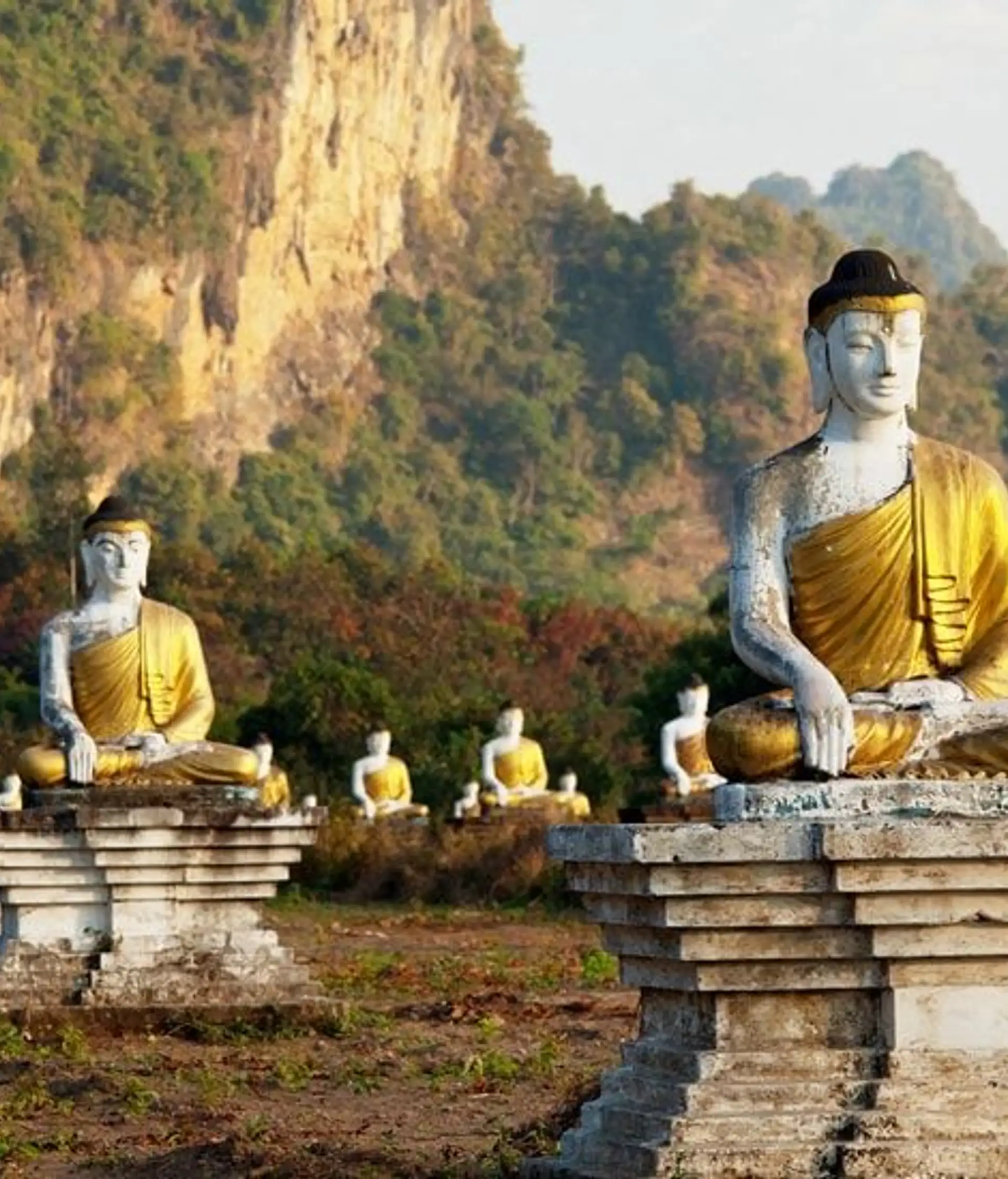 Travel in Asia - Rows of seated Buddha statues in a grassy landscape with rocky hills in the background in Southern Myanmar (Burma)
