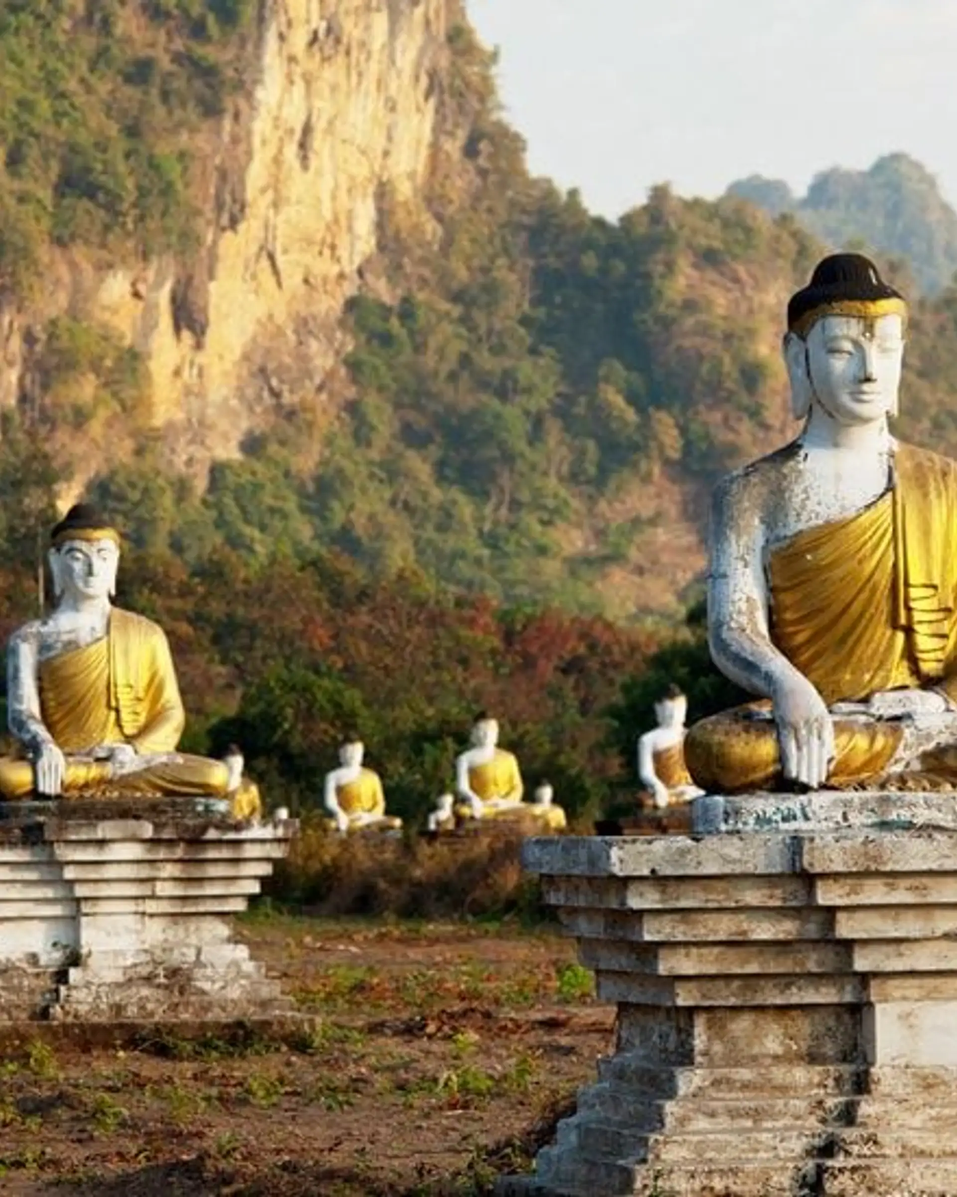 Travel in Asia - Rows of seated Buddha statues in a grassy landscape with rocky hills in the background in Southern Myanmar (Burma)