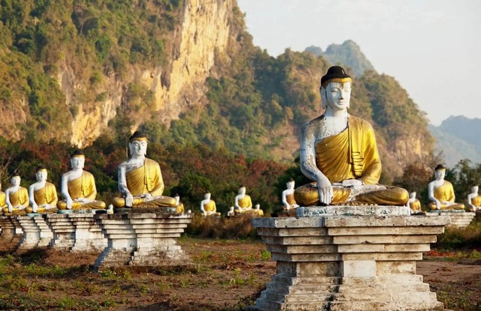 Travel in Asia - Rows of seated Buddha statues in a grassy landscape with rocky hills in the background in Southern Myanmar (Burma)