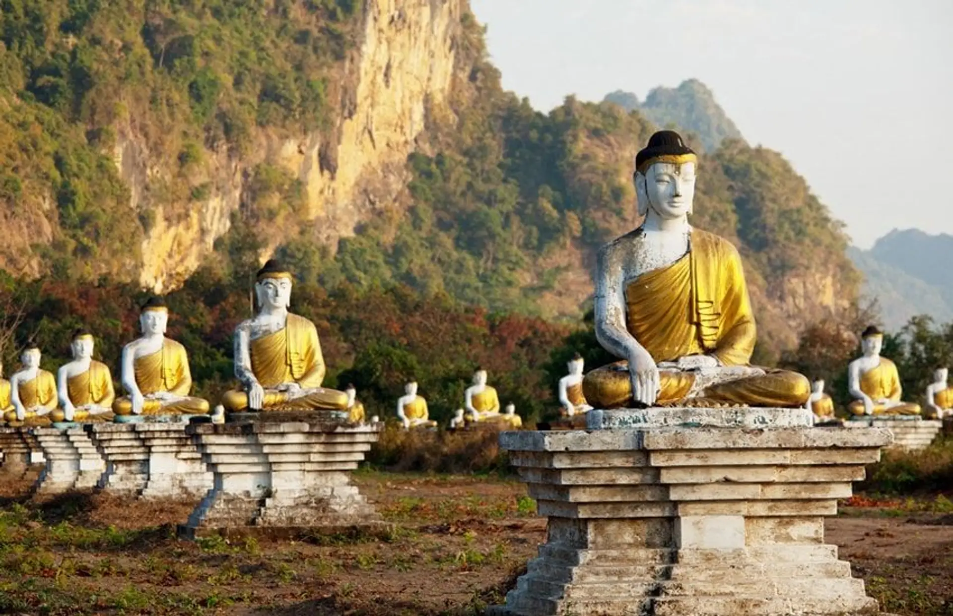 Travel in Asia - Rows of seated Buddha statues in a grassy landscape with rocky hills in the background in Southern Myanmar (Burma)