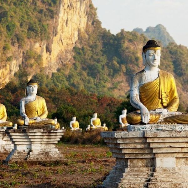 Travel in Asia - Rows of seated Buddha statues in a grassy landscape with rocky hills in the background in Southern Myanmar (Burma)