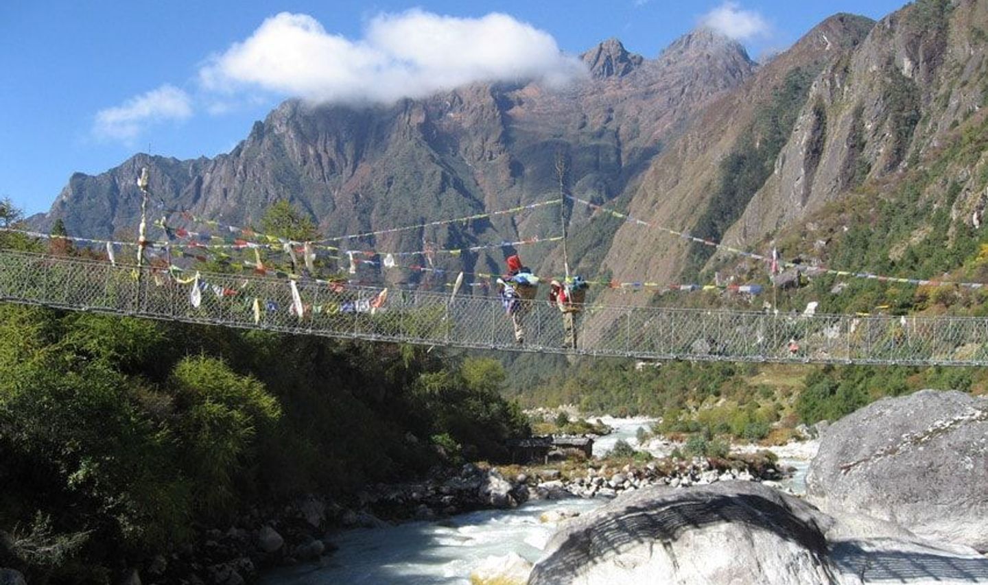 Travel in Asia - People traversing a rope bridge suspended above a rushing river, dramatic Himalayan mountains in the background