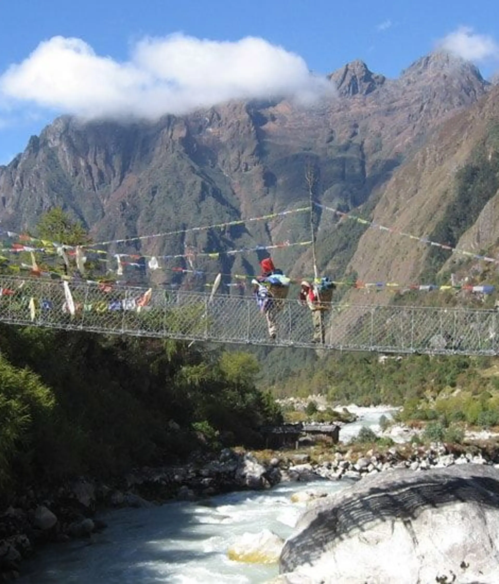 Travel in Asia - People traversing a rope bridge suspended above a rushing river, dramatic Himalayan mountains in the background