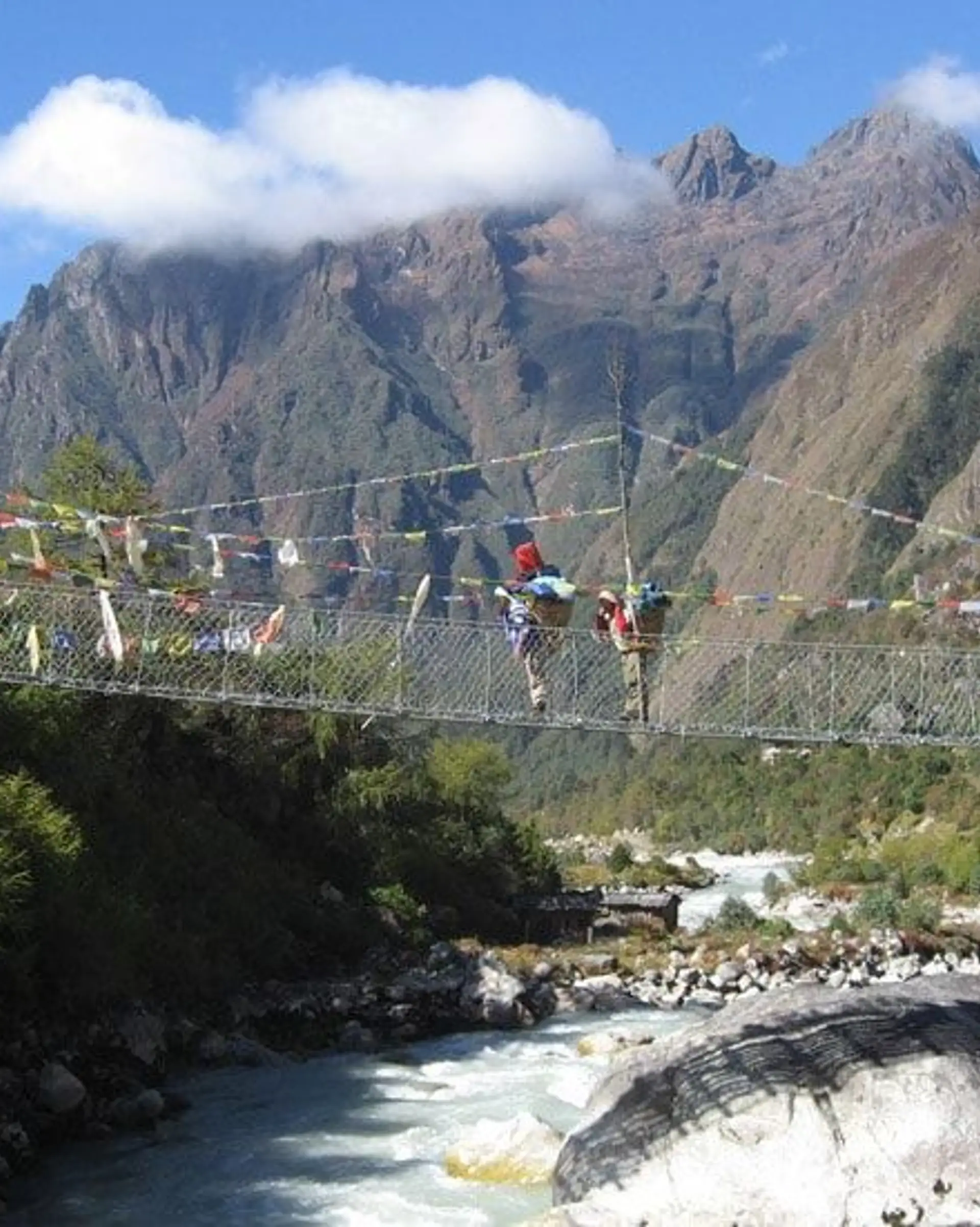 Travel in Asia - People traversing a rope bridge suspended above a rushing river, dramatic Himalayan mountains in the background
