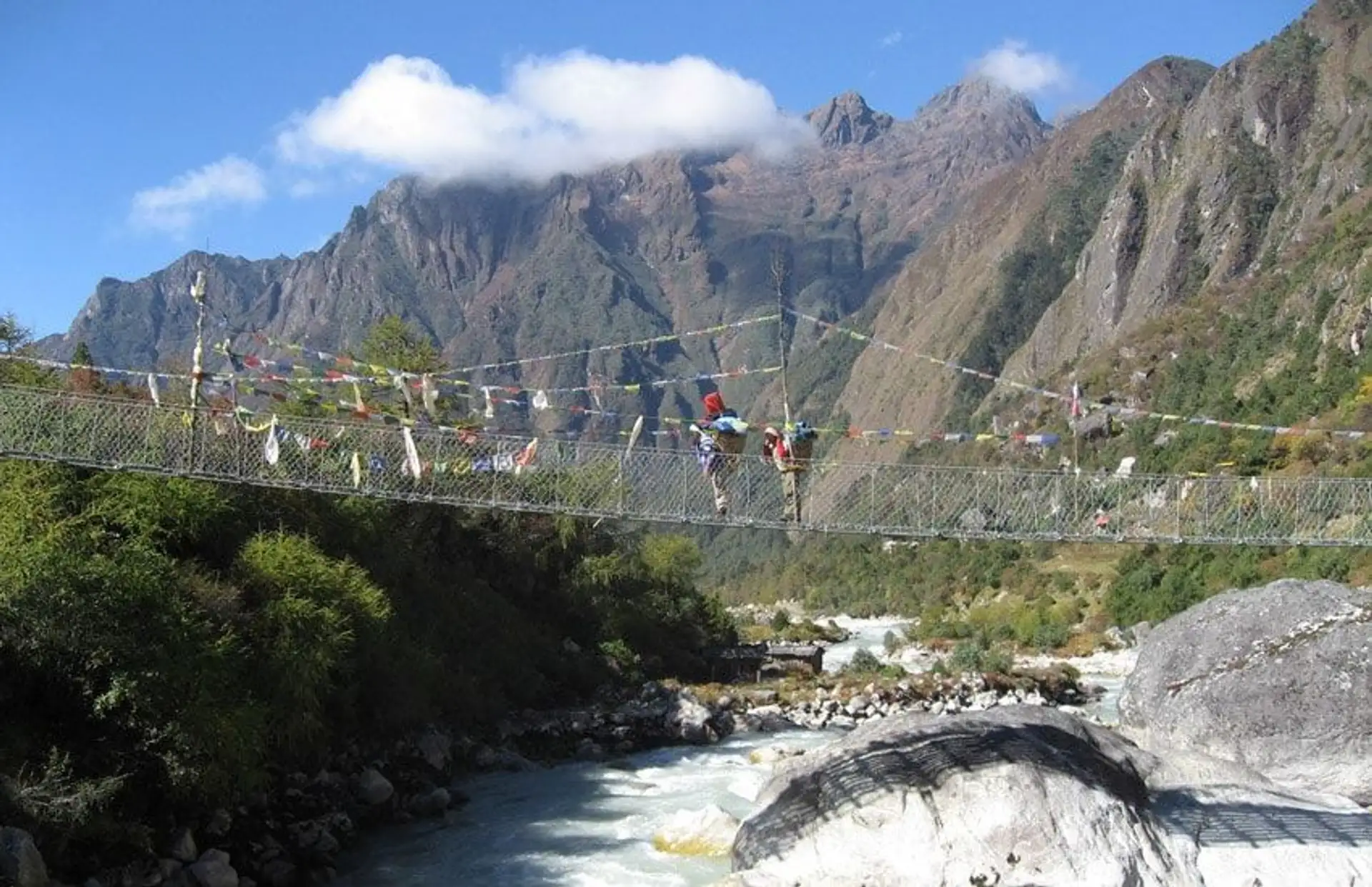 Travel in Asia - People traversing a rope bridge suspended above a rushing river, dramatic Himalayan mountains in the background