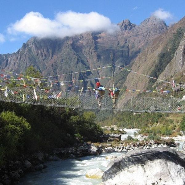 Travel in Asia - People traversing a rope bridge suspended above a rushing river, dramatic Himalayan mountains in the background