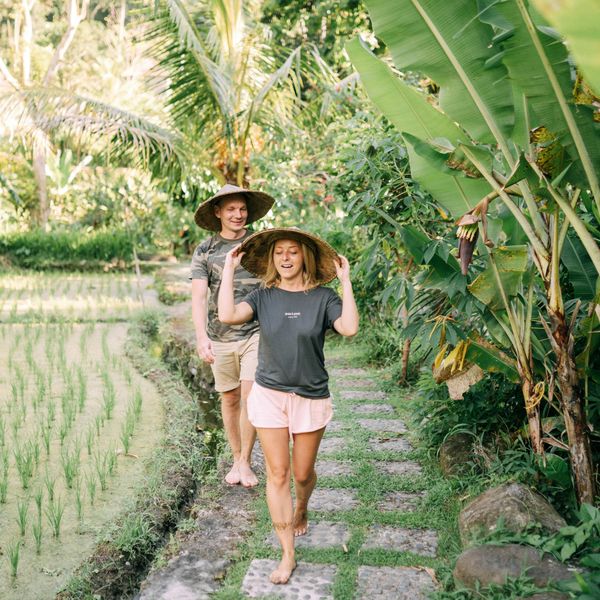 Travel in Asia - A young couple walking on a stone path between a rice field and tropical plants wearing hats